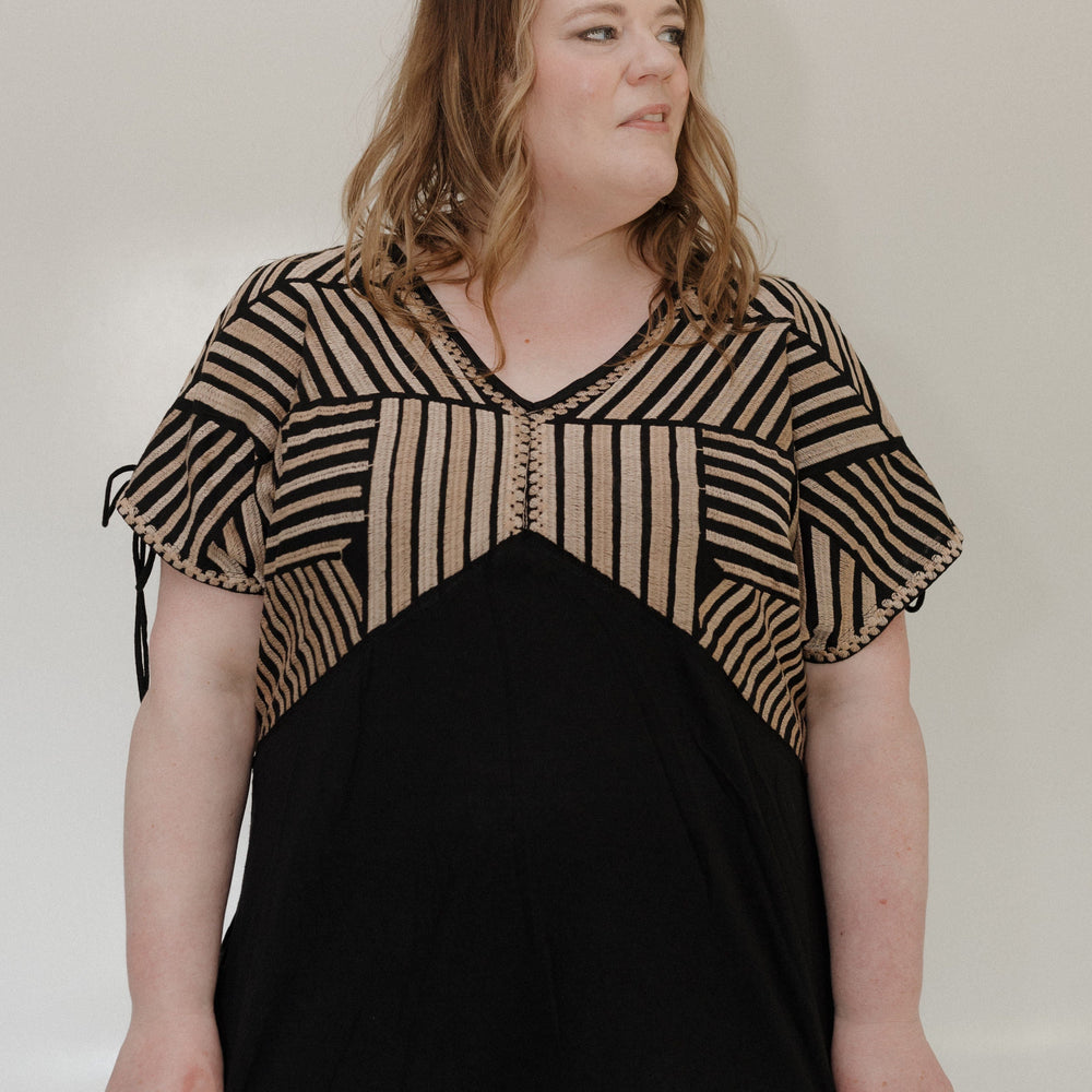Woman wearing a black and beige striped top against a plain background