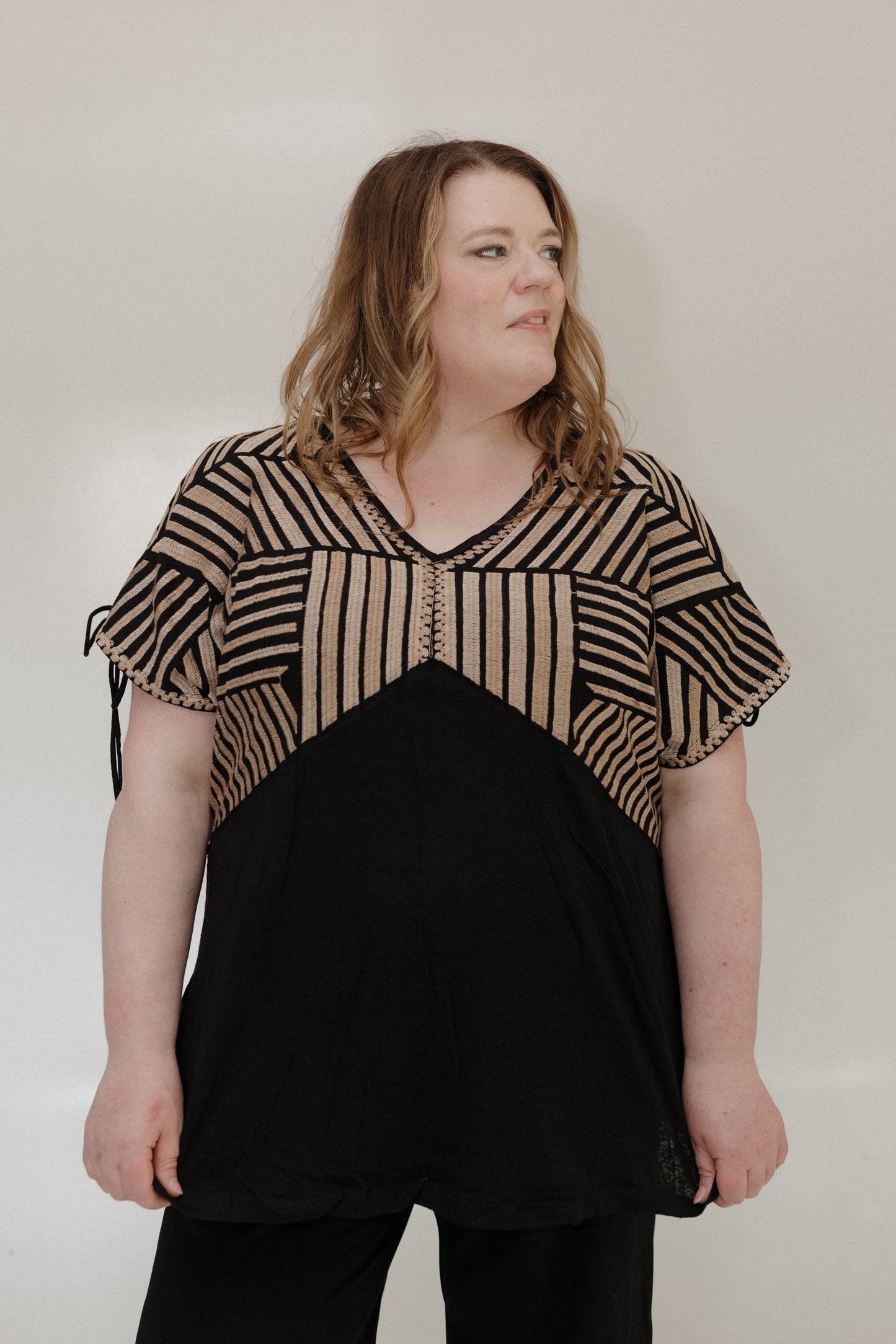 Woman wearing a black and beige striped top against a plain background