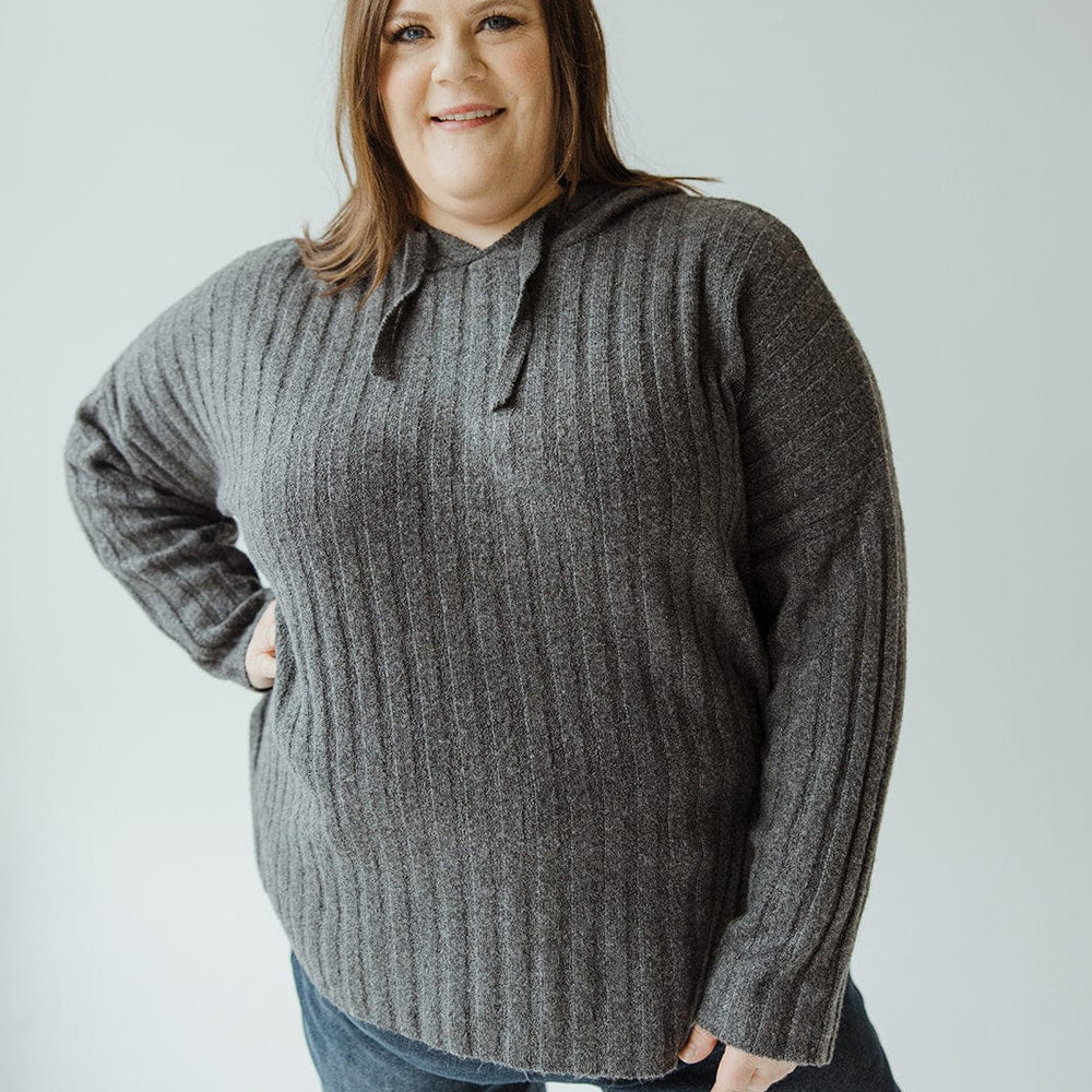 A woman stands against a plain background, wearing the LINEAR ATHLEISURE HOODIE by Yesta and blue jeans, smiling with one hand on her hip.