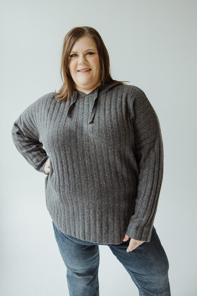 A woman stands against a plain background, wearing the LINEAR ATHLEISURE HOODIE by Yesta and blue jeans, smiling with one hand on her hip.