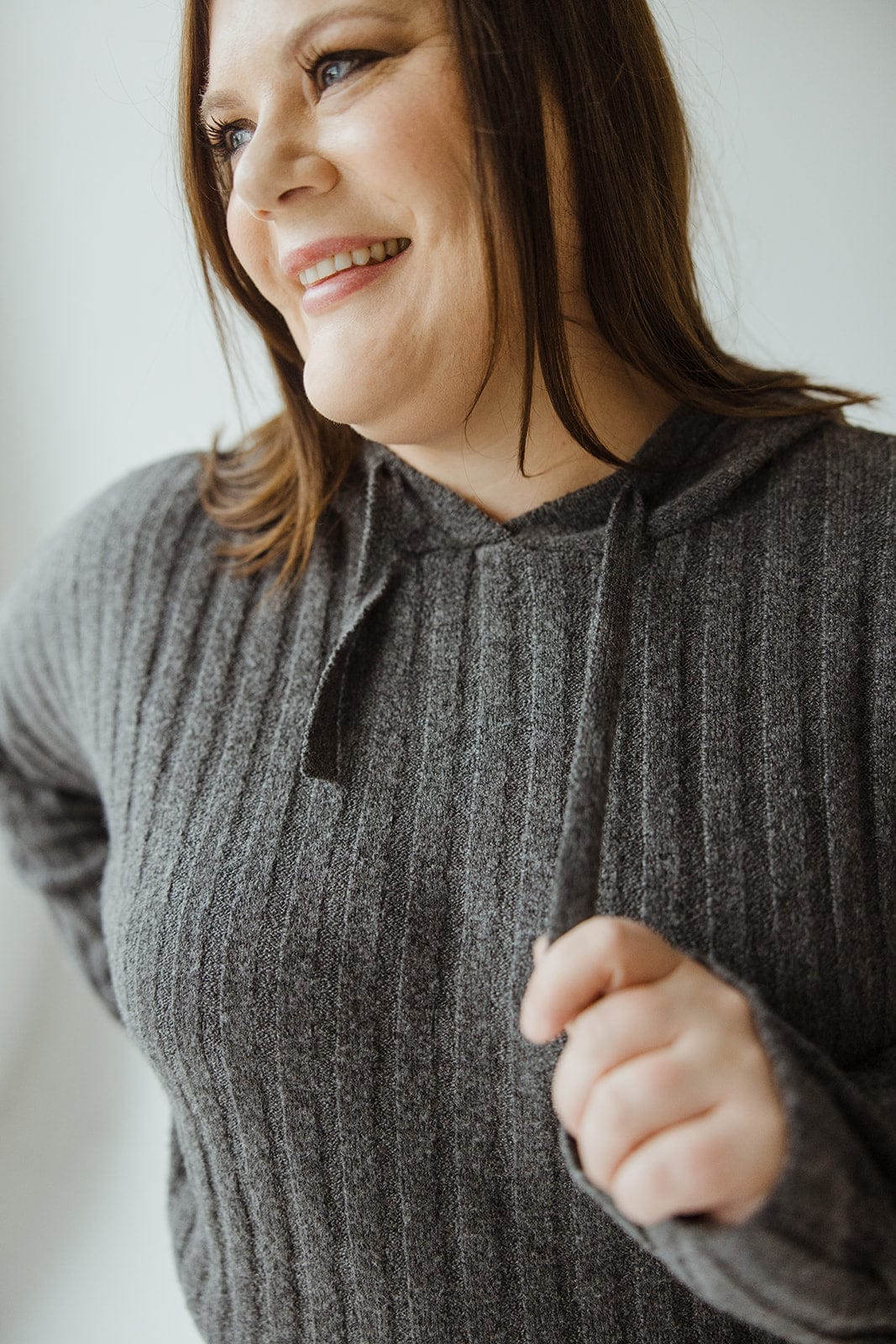 A woman with medium-length brown hair smiles while wearing a LINEAR ATHLEISURE HOODIE by Yesta, embracing an elevated fashion look.