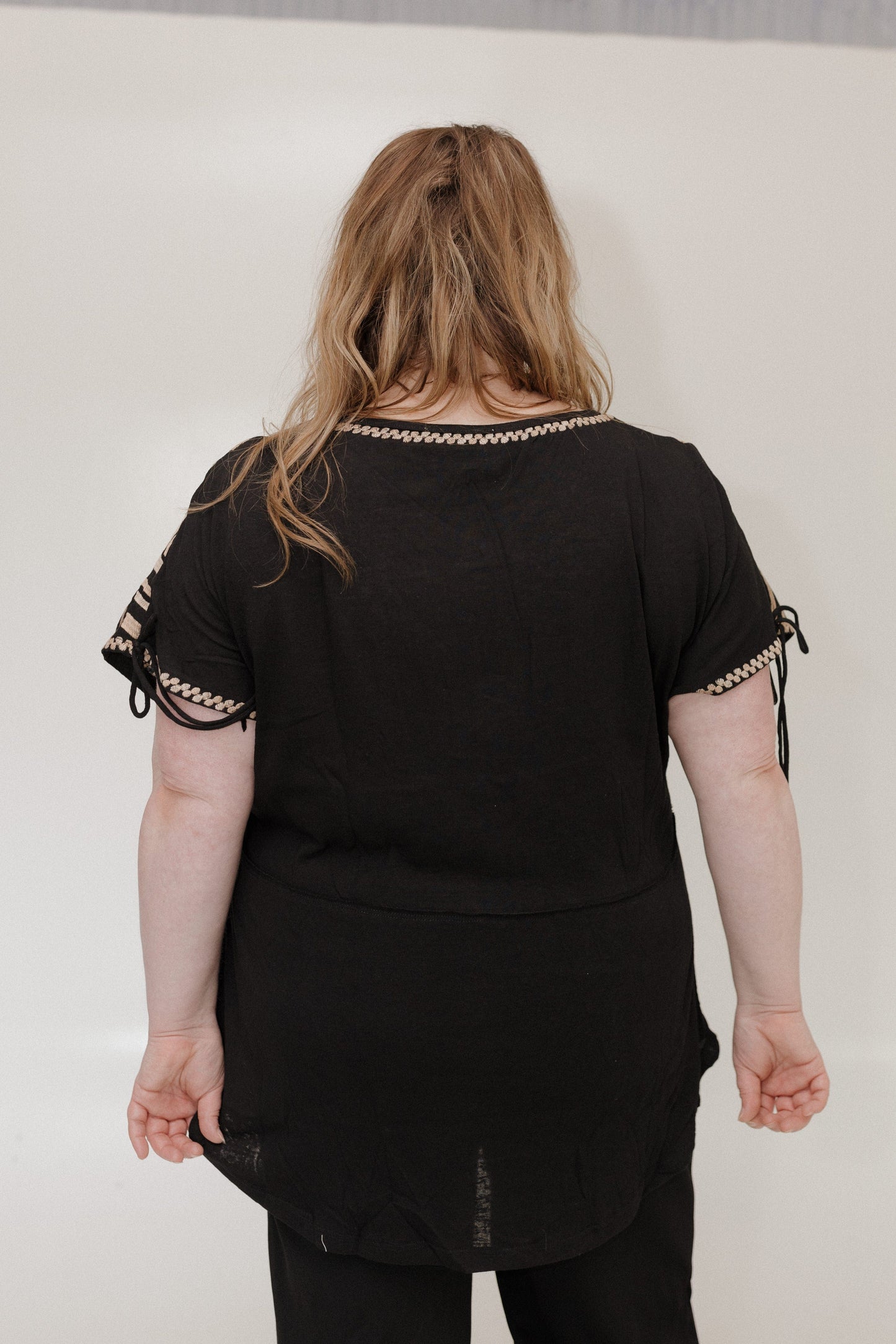 Person wearing a black top with embroidered details on sleeves against a white background