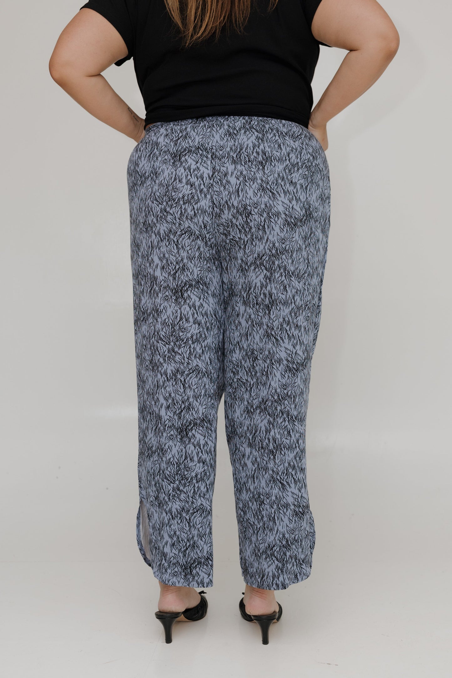 Person wearing a black top and patterned gray pants on a plain background