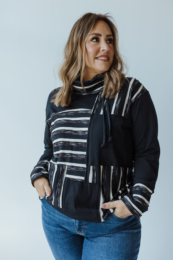 A woman with shoulder-length hair stands against a plain background, wearing the neon buddha LONG-SLEEVE ROUND NECK TUNIC WITH STRIPE DETAIL IN BLACK and blue jeans, with her hands in her pockets.