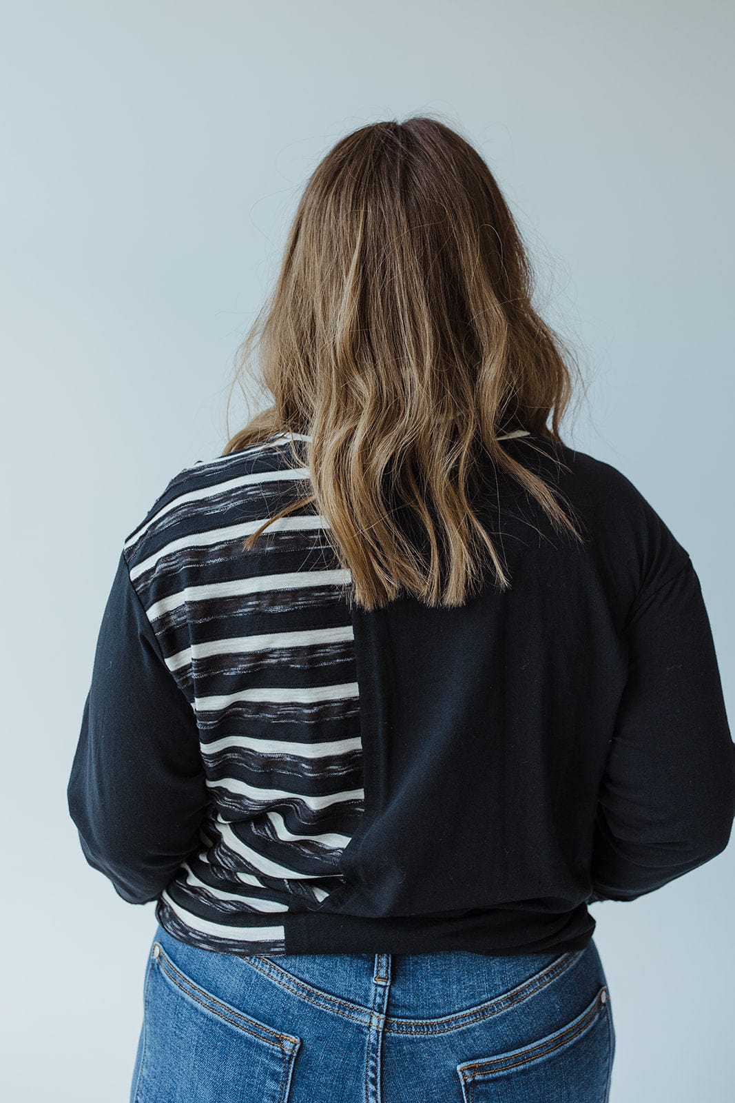A person with light brown wavy hair stands with their back to the camera, wearing a 