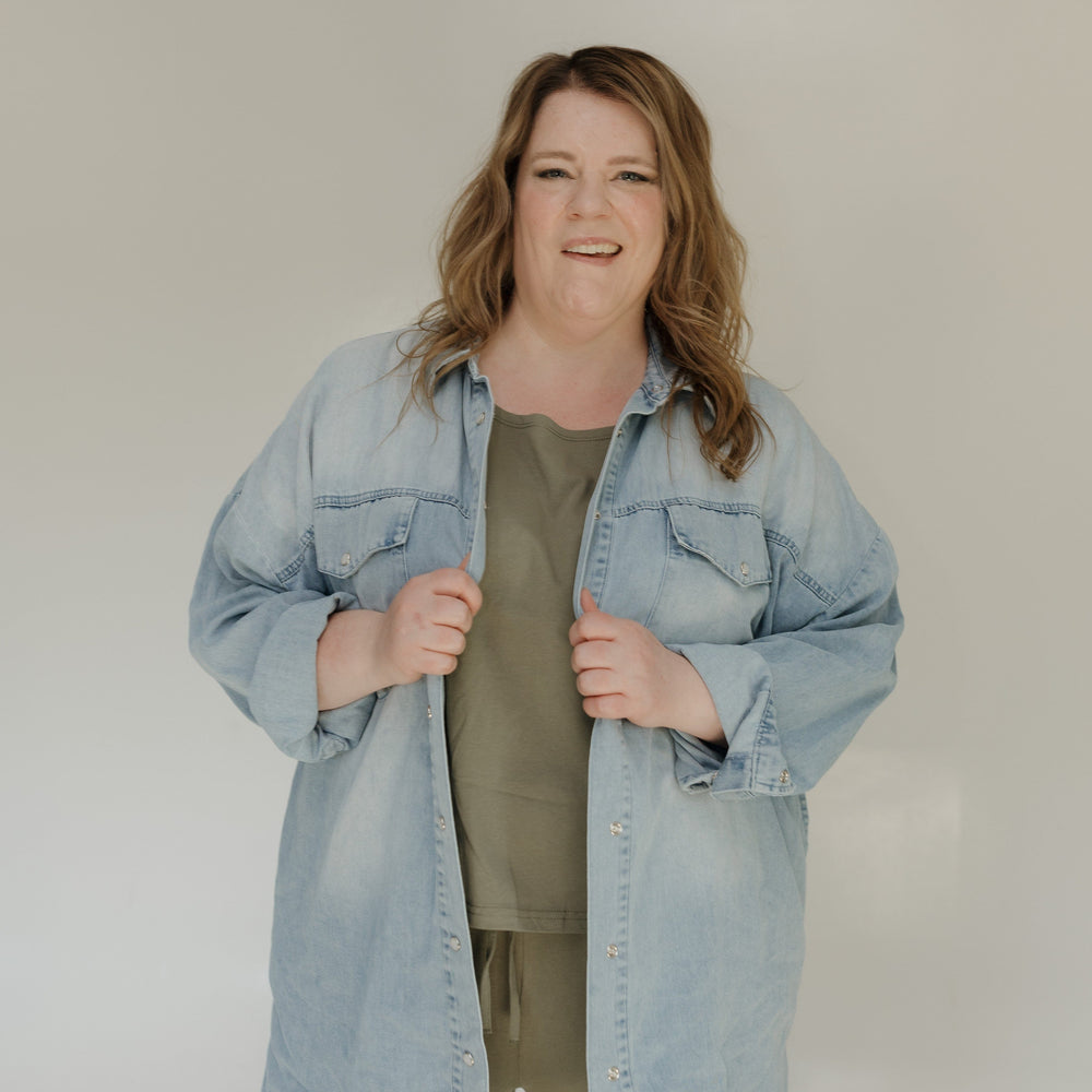 Woman wearing a light blue denim jacket over a green shirt against a white background