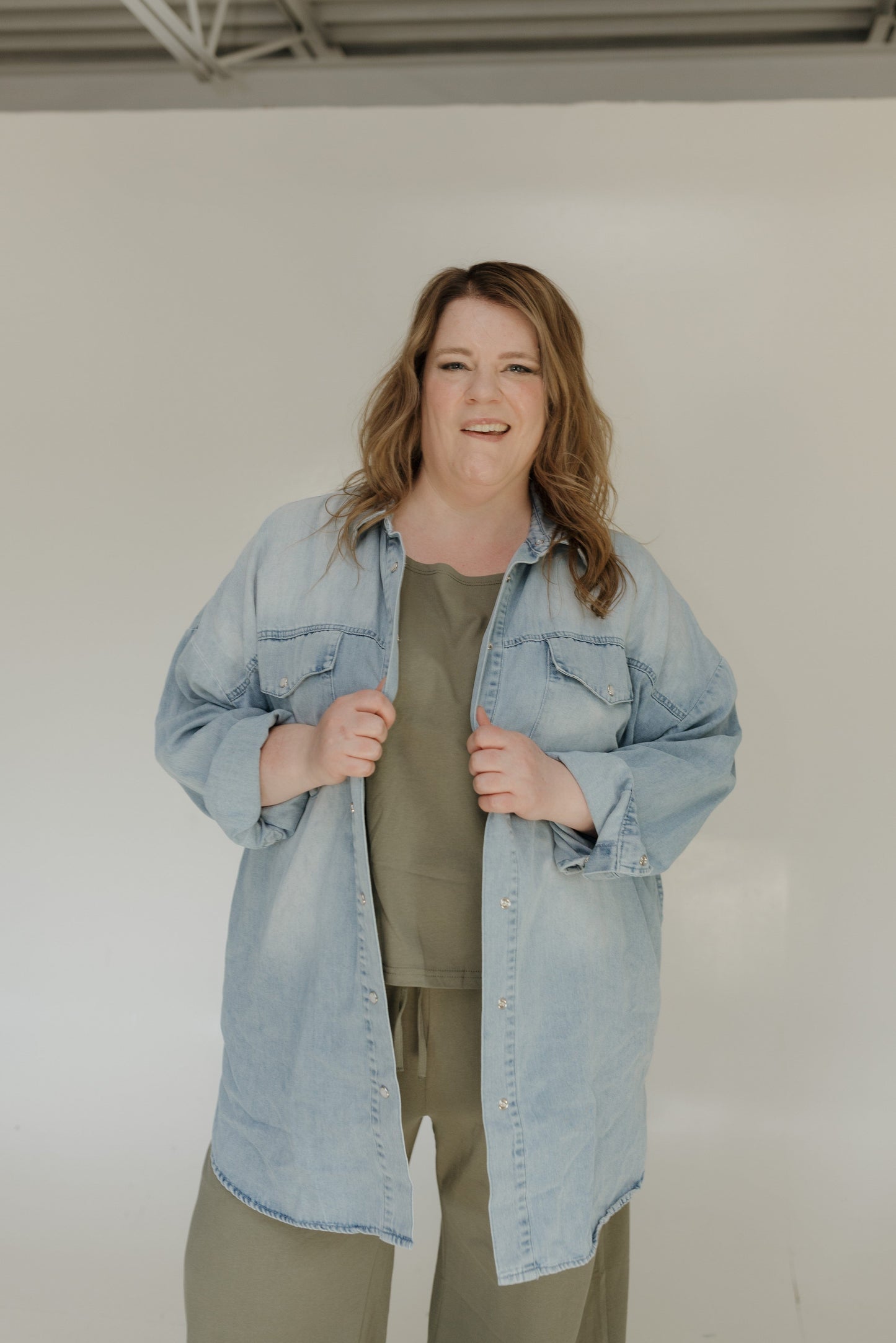 Woman wearing a light blue denim jacket over a green shirt against a white background