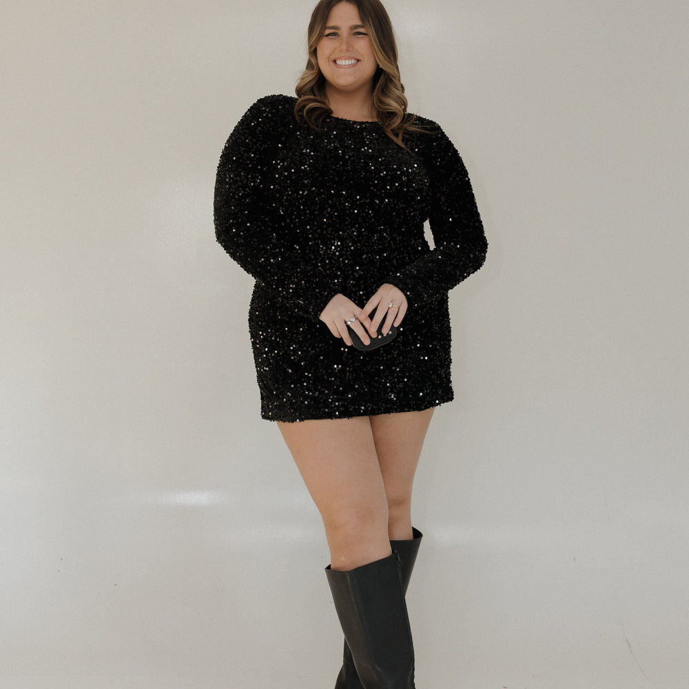 Woman wearing a black sparkly dress and knee-high boots against a white background