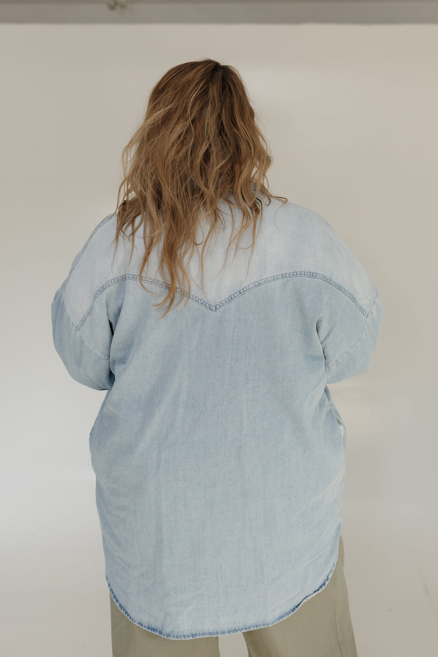 Person wearing a light blue denim shirt against a plain background