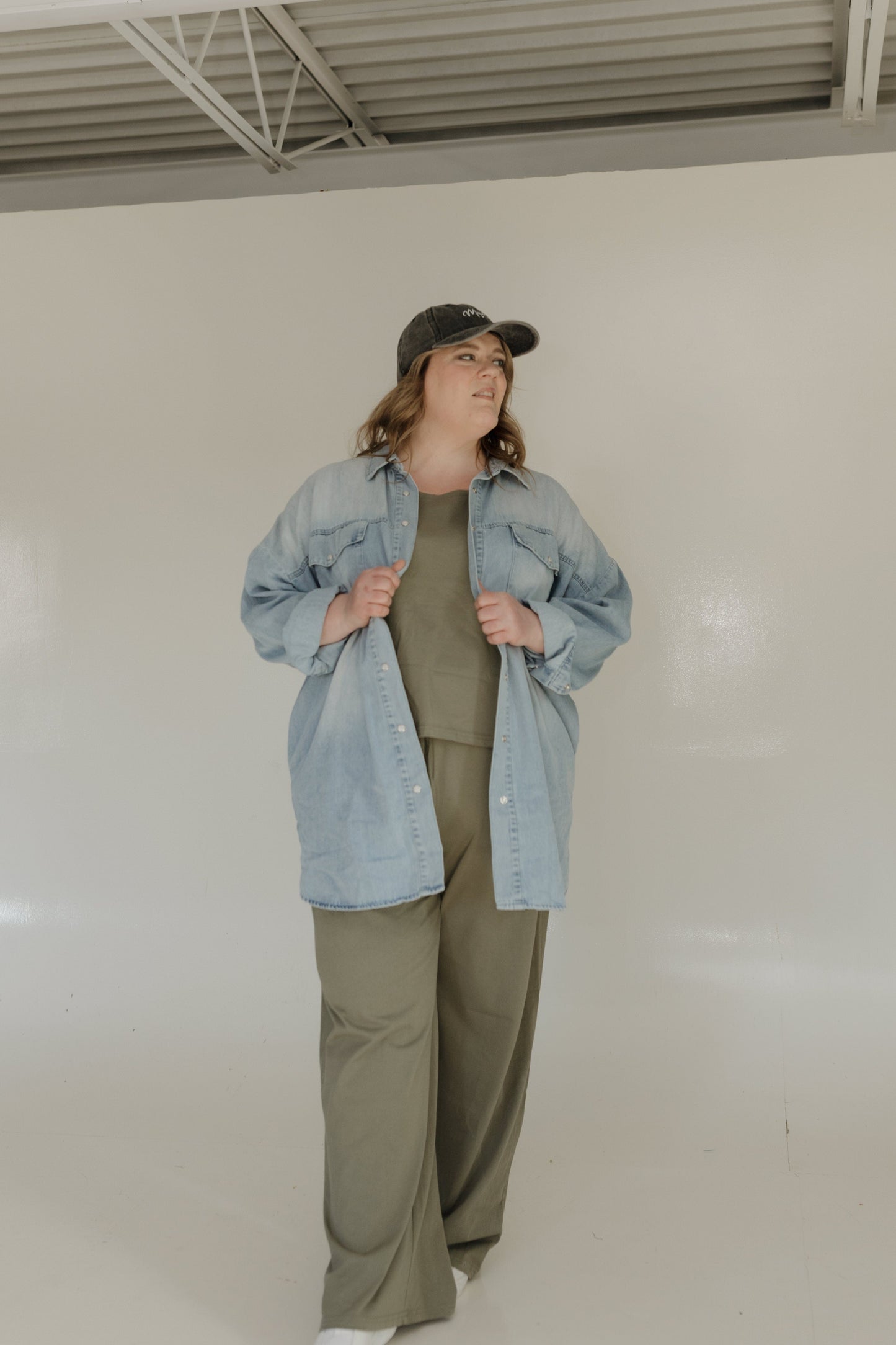 Person wearing a denim jacket, green shirt, and pants against a plain background