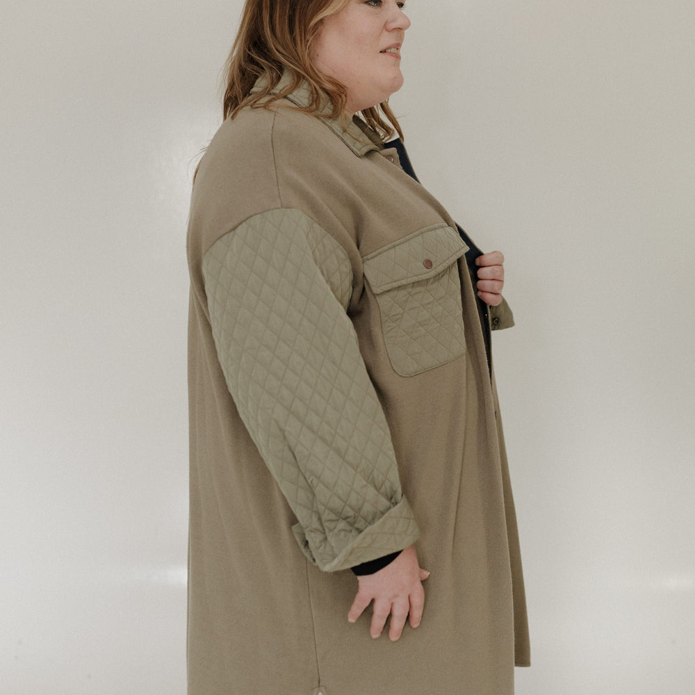Woman wearing a long olive green jacket against a plain background