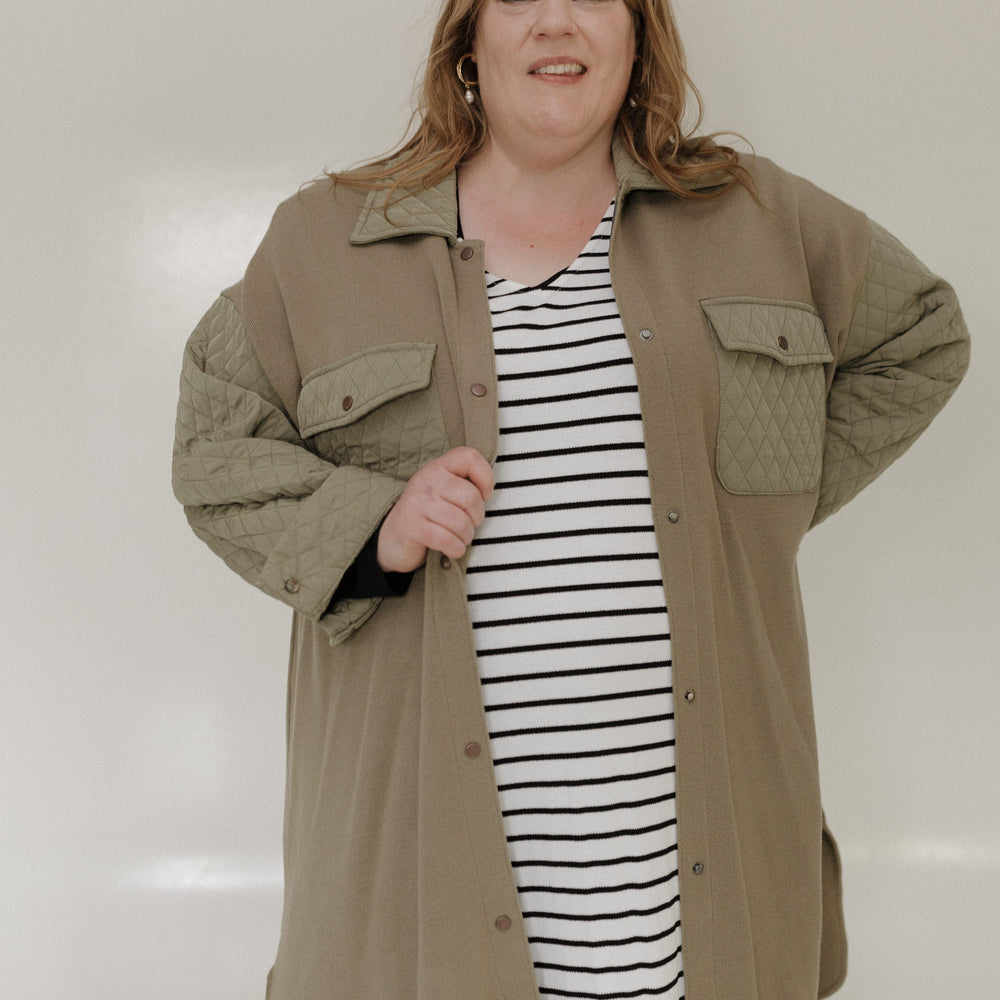 Woman wearing a beige jacket over a striped dress against a plain background
