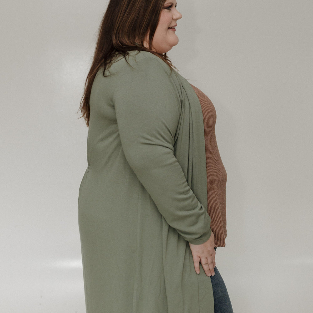 Woman wearing a green cardigan over a brown top on a plain background