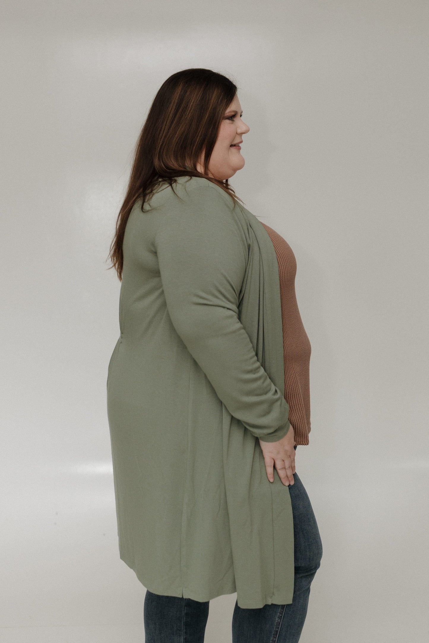 Woman wearing a green cardigan over a brown top on a plain background