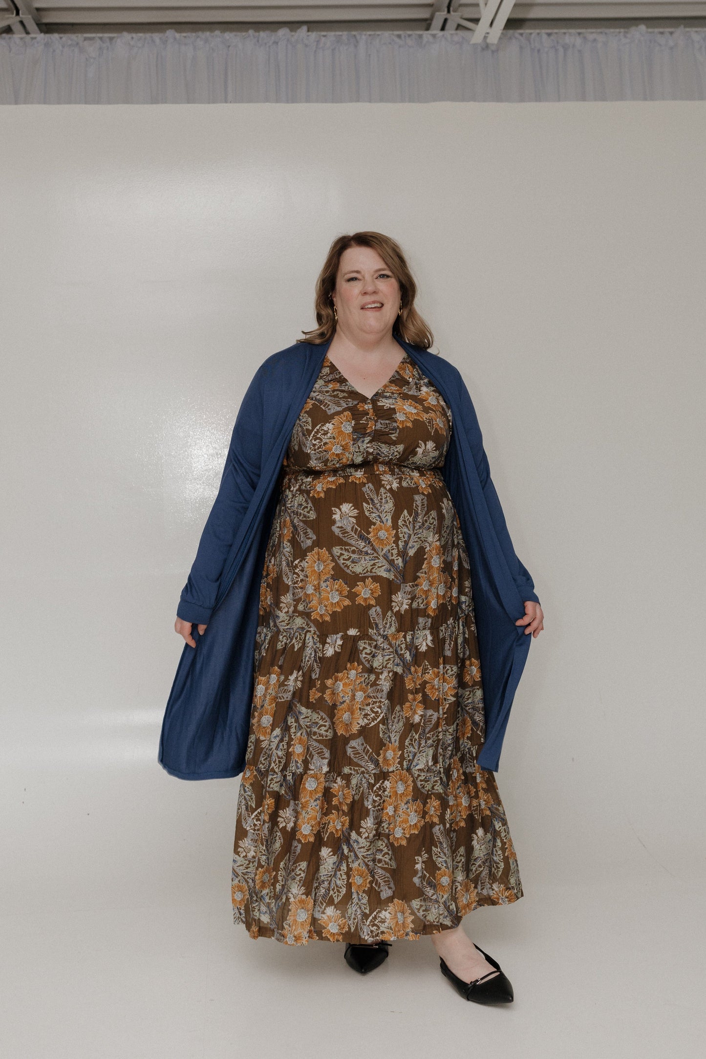 Woman wearing a floral dress and blue cardigan against a white background