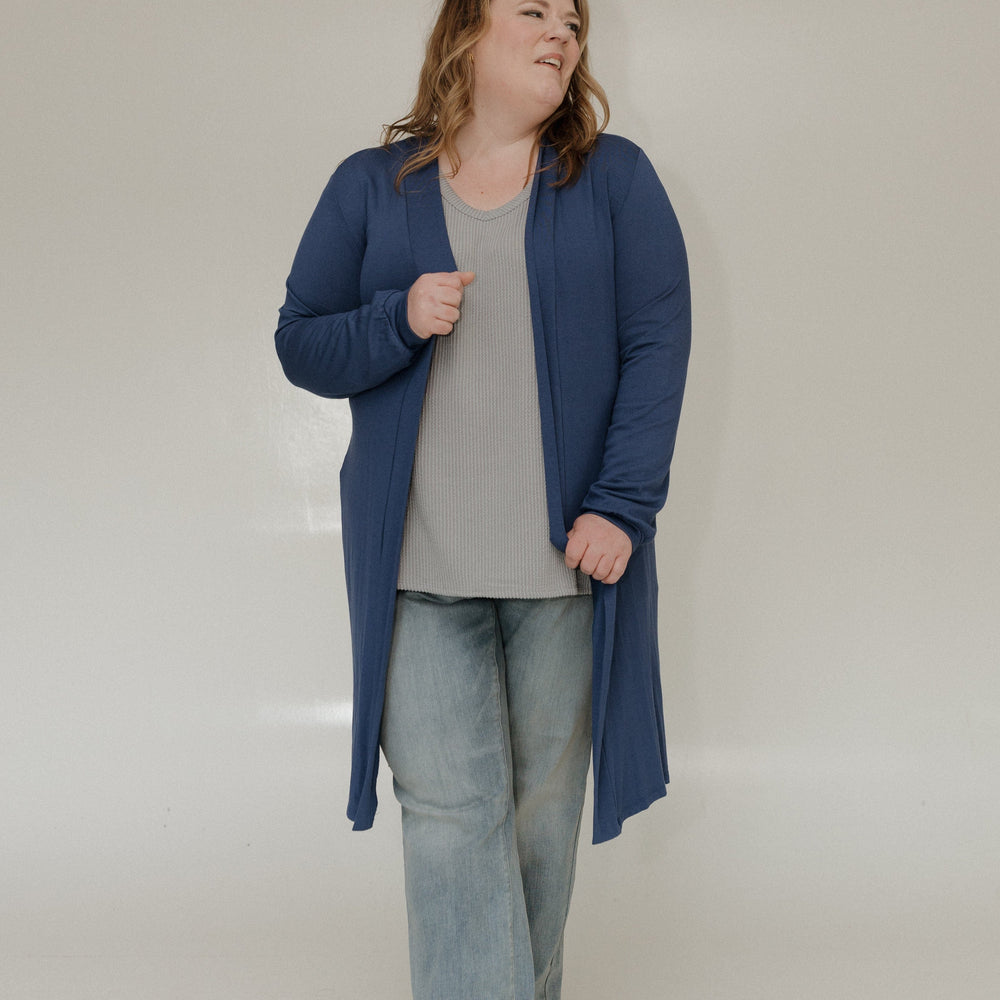 Person wearing a blue cardigan, gray shirt, and light blue jeans on a white background