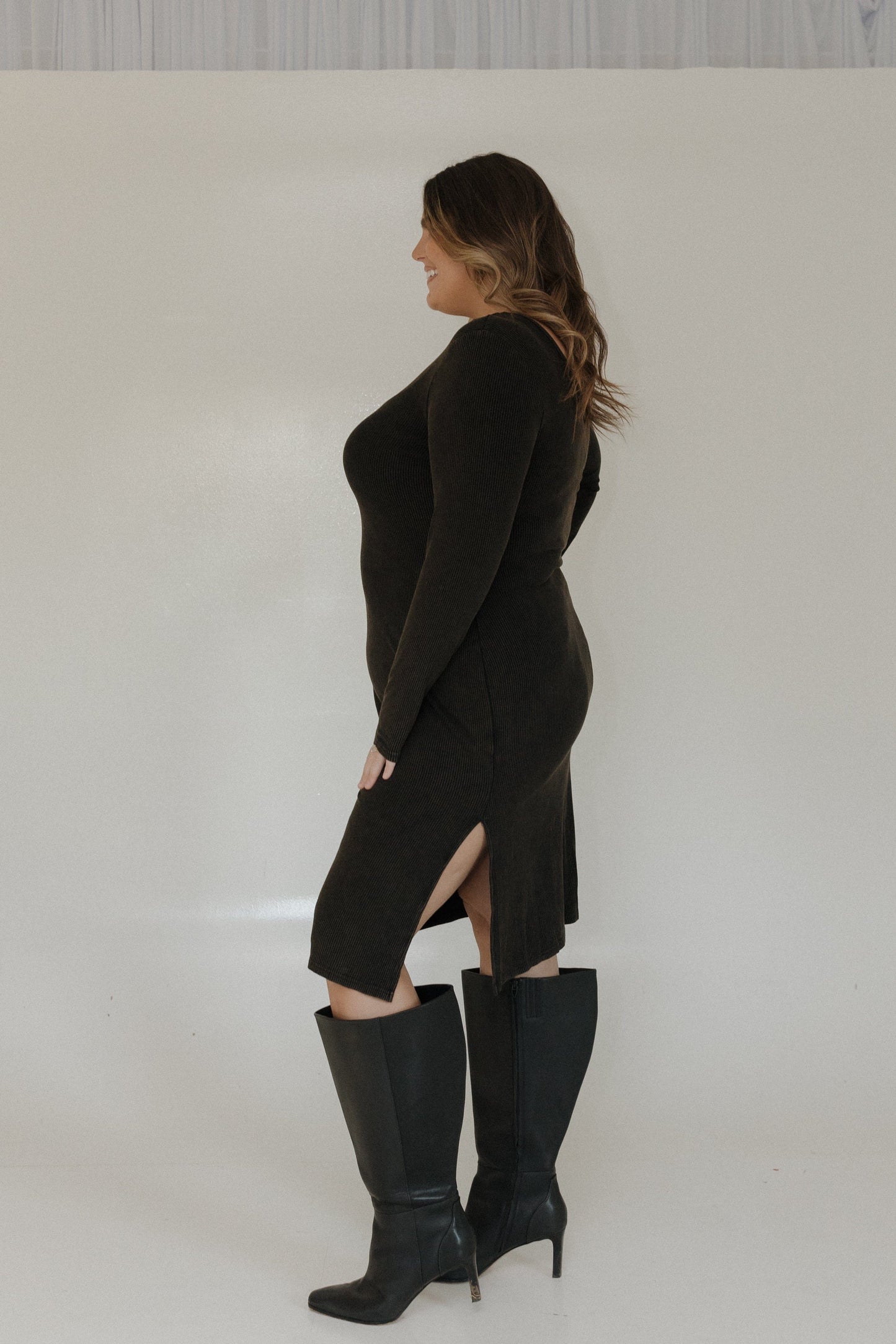 Woman wearing a black dress with a slit and black knee-high boots on a white background