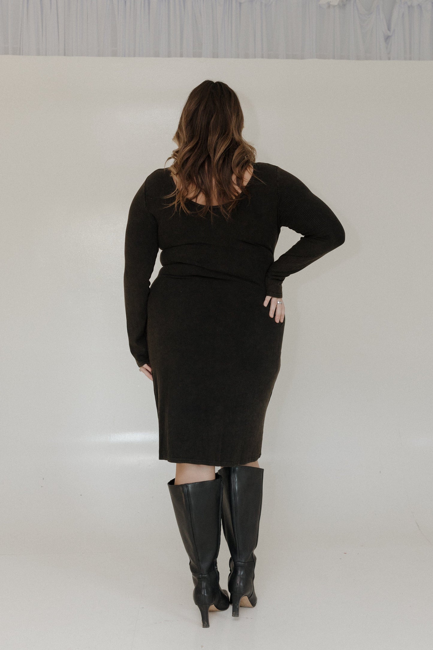 Person wearing a black outfit with knee-high boots on a plain background