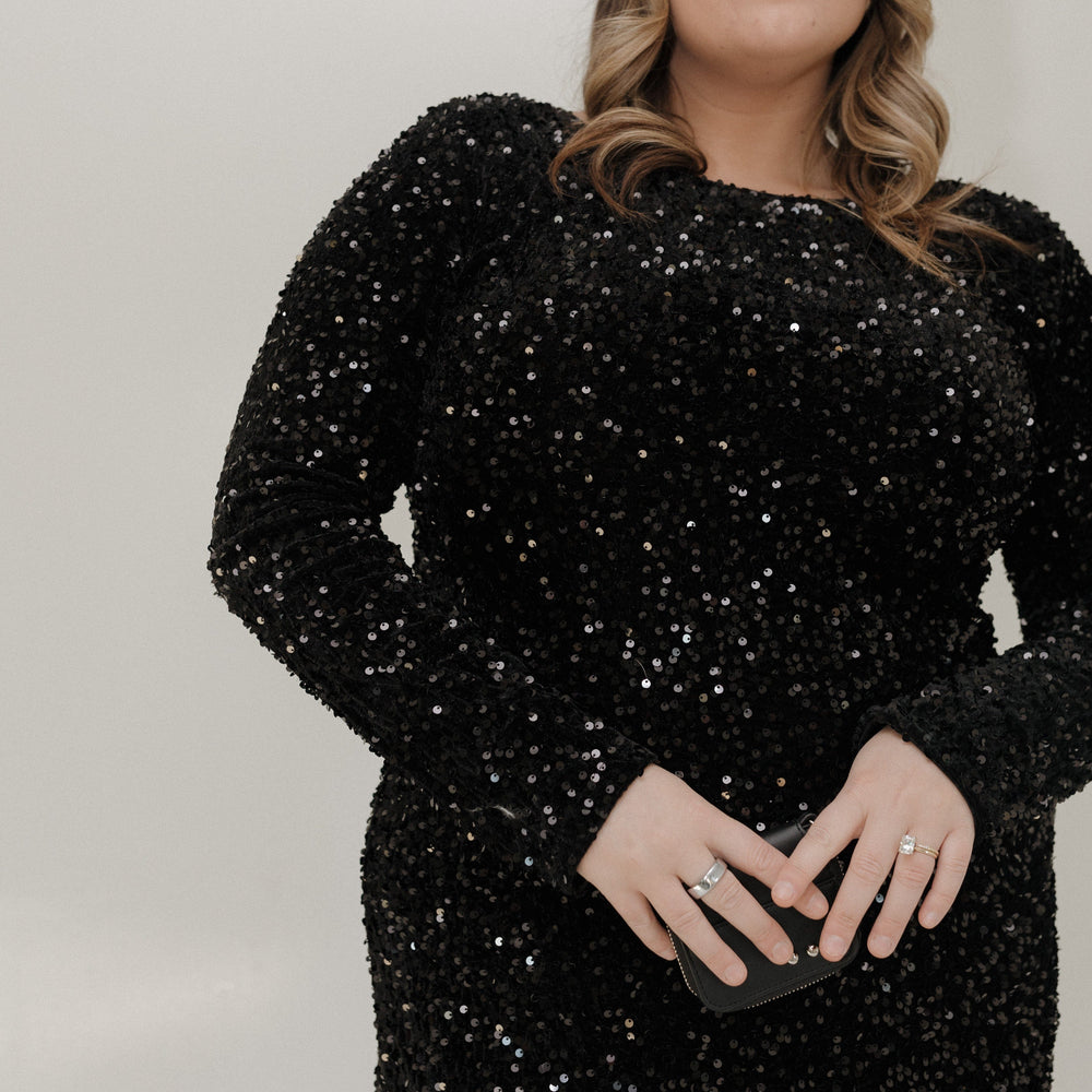 Woman wearing a black sequin dress against a plain background