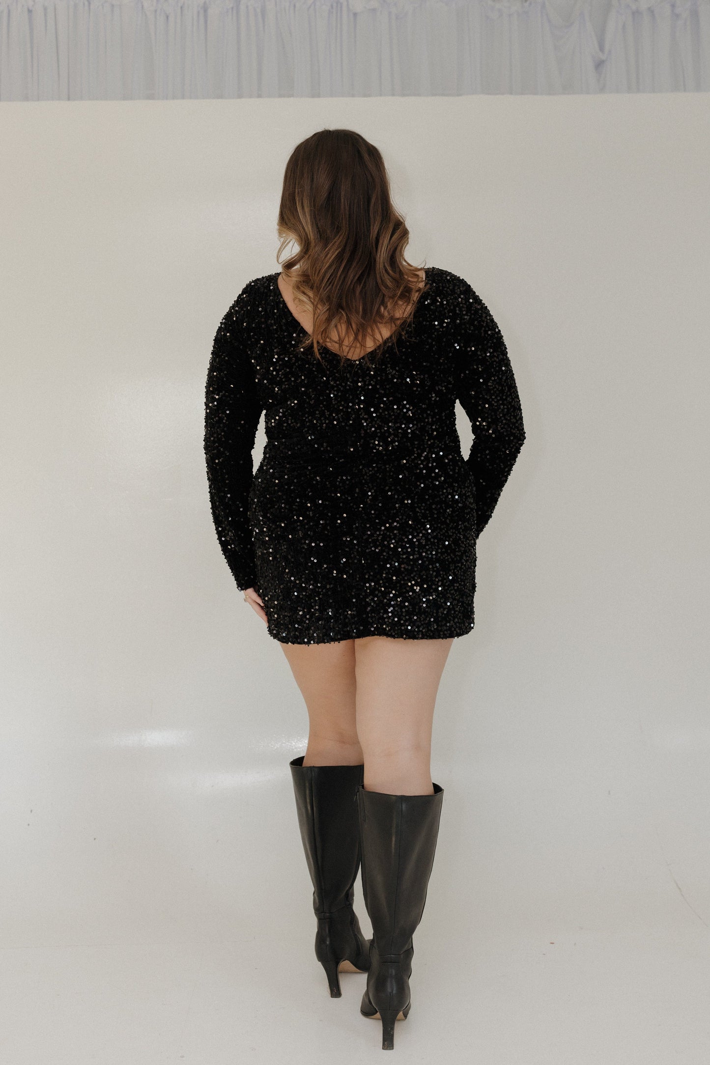 Person wearing a black sequin dress and black knee-high boots on a white background