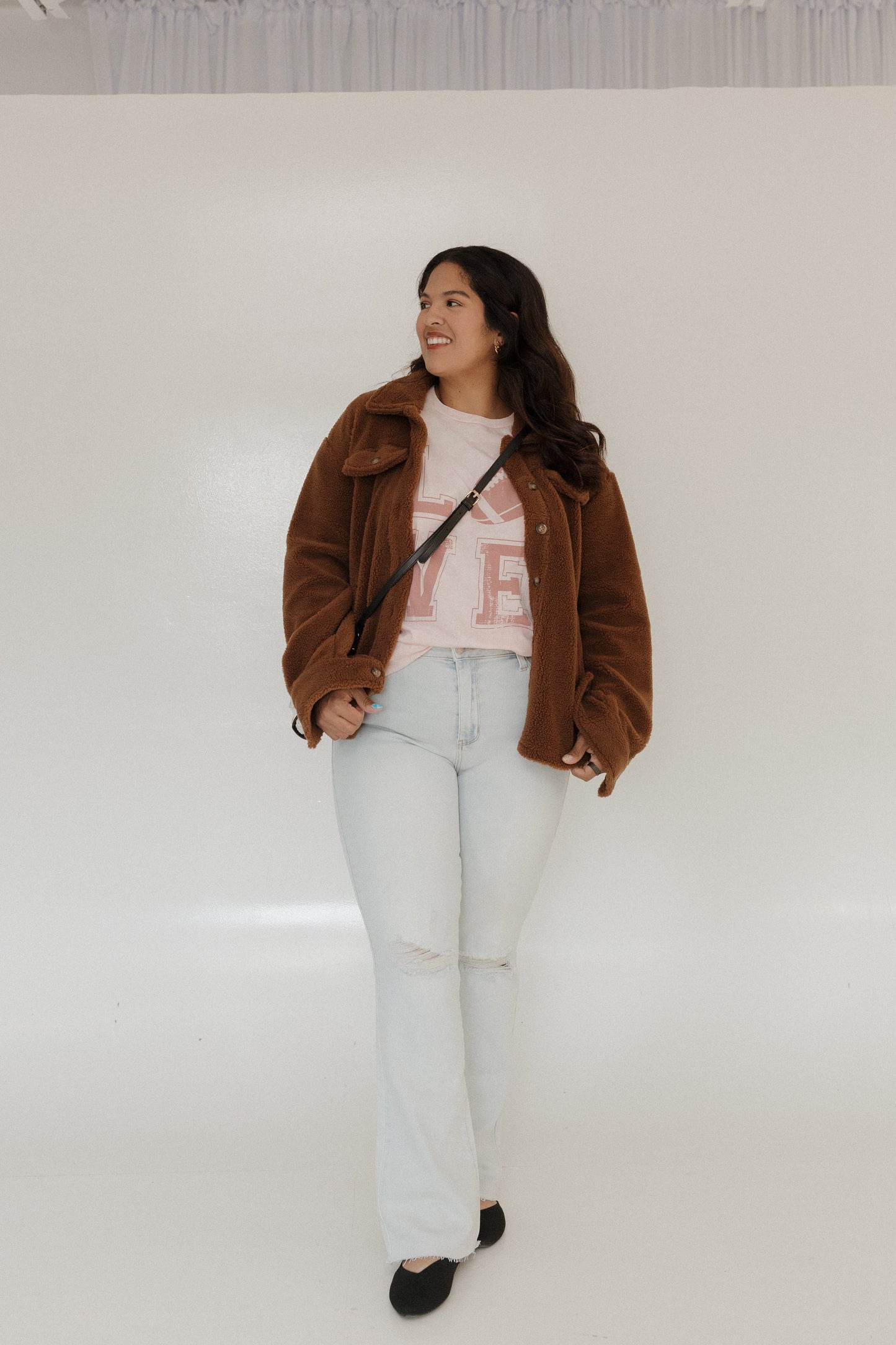 "LOVE" FOOTBALL GRAPHIC TEE IN LIGHT BLUSH MINERAL WASH Woman wearing a pink 'LOVE' t-shirt with a football graphic on a plain A person stands smiling in a Love Marlow "LOVE" FOOTBALL GRAPHIC TEE IN LIGHT BLUSH MINERAL WASH, paired with blue pants and flip-flops, posing against a plain background.