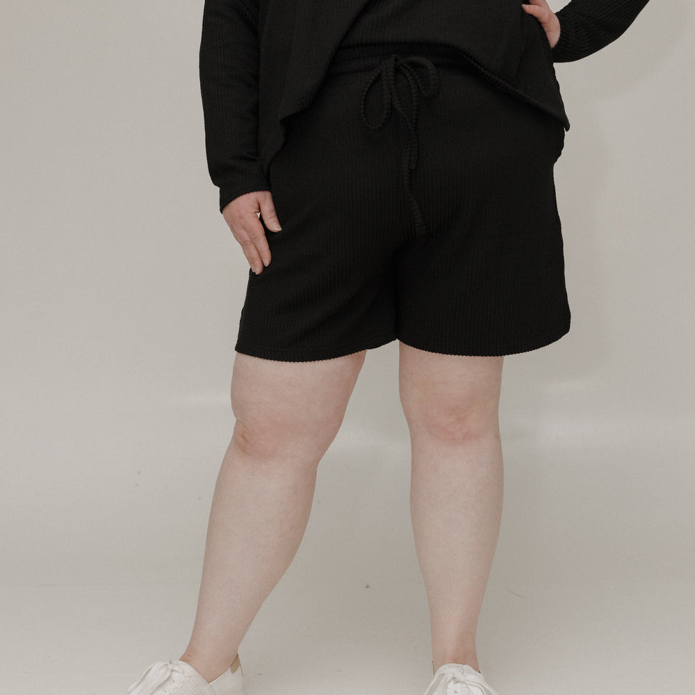 Person wearing a black outfit with shorts on a plain background