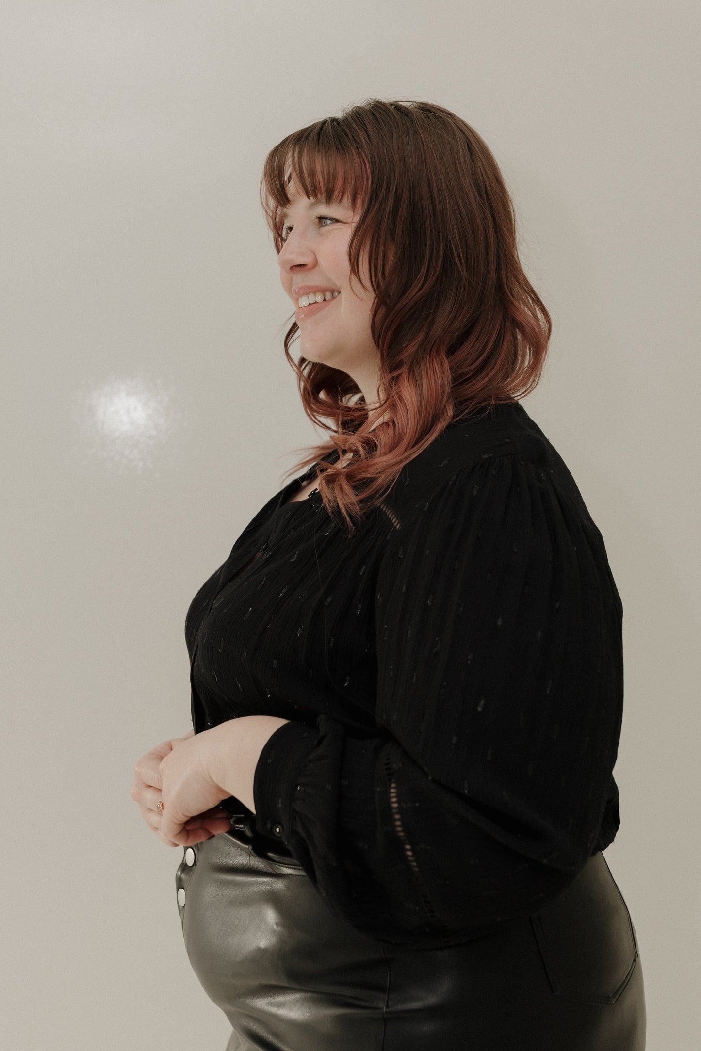Woman with shoulder-length hair wearing a black top and leather pants against a plain background
