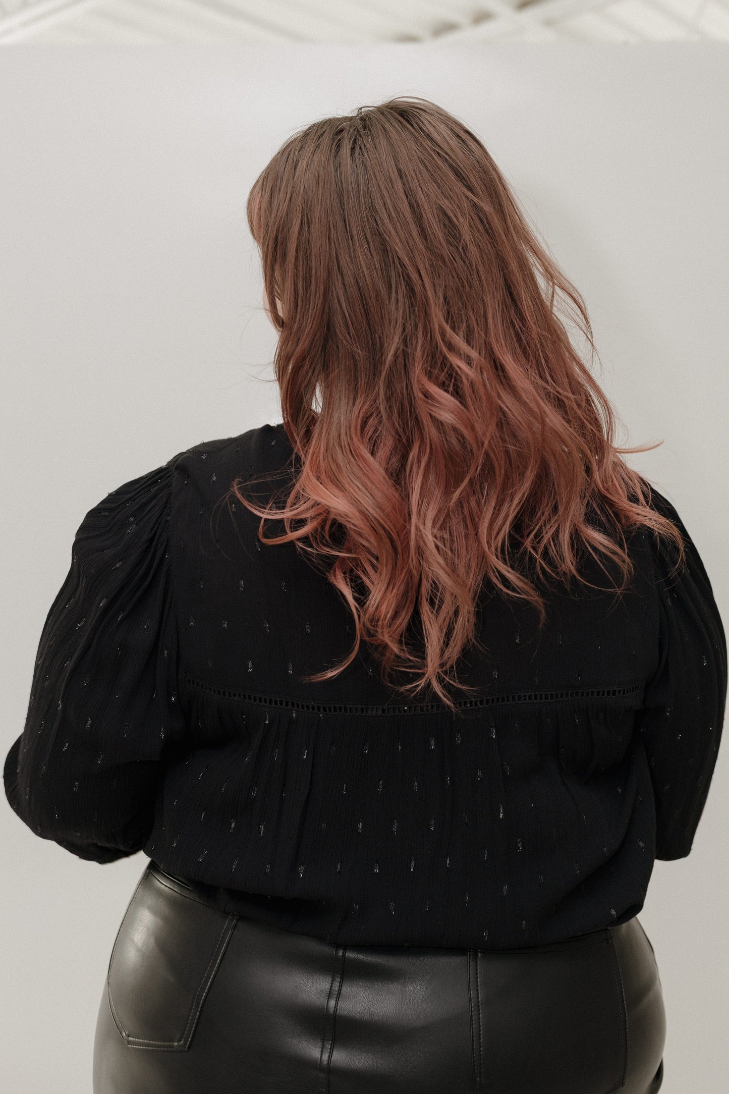 Person wearing a black top with puffed sleeves and a leather skirt, standing against a white background.