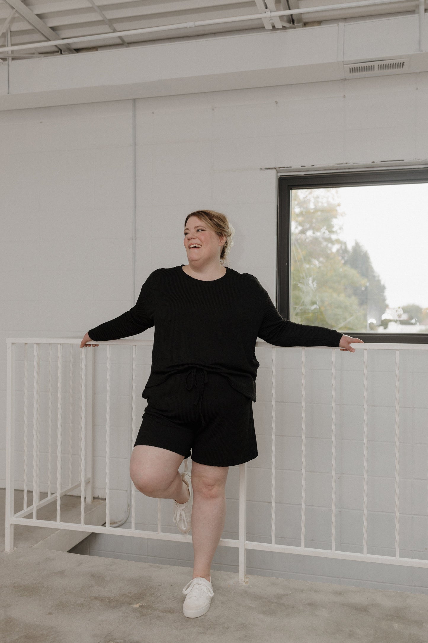 Person in black outfit standing in a modern indoor setting with white walls and a large window.