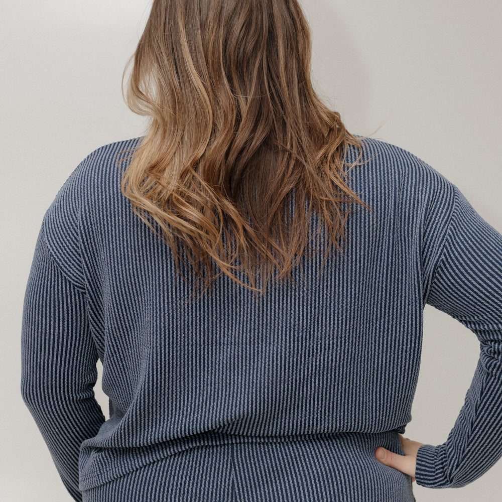 Person wearing a blue ribbed sweater and skirt set against a plain background