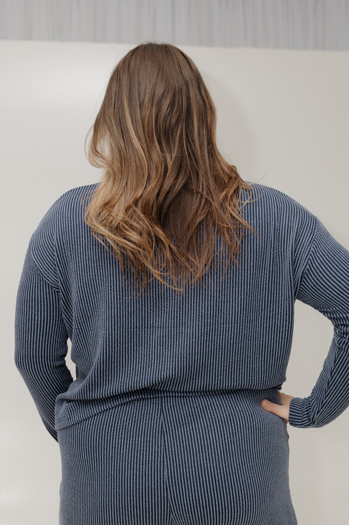 Person wearing a blue ribbed sweater and skirt set against a plain background