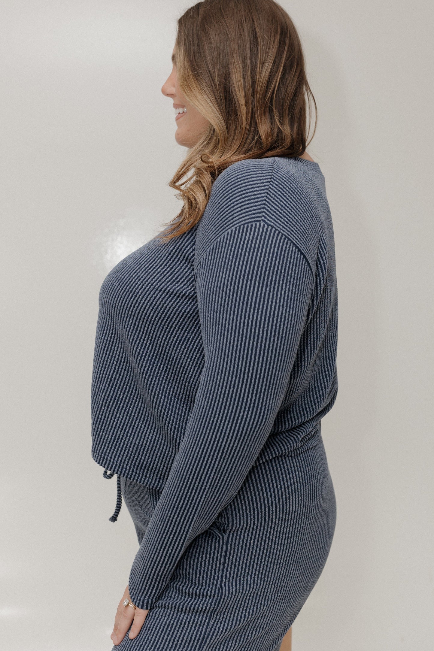 Woman wearing a gray ribbed sweater and pants against a plain background