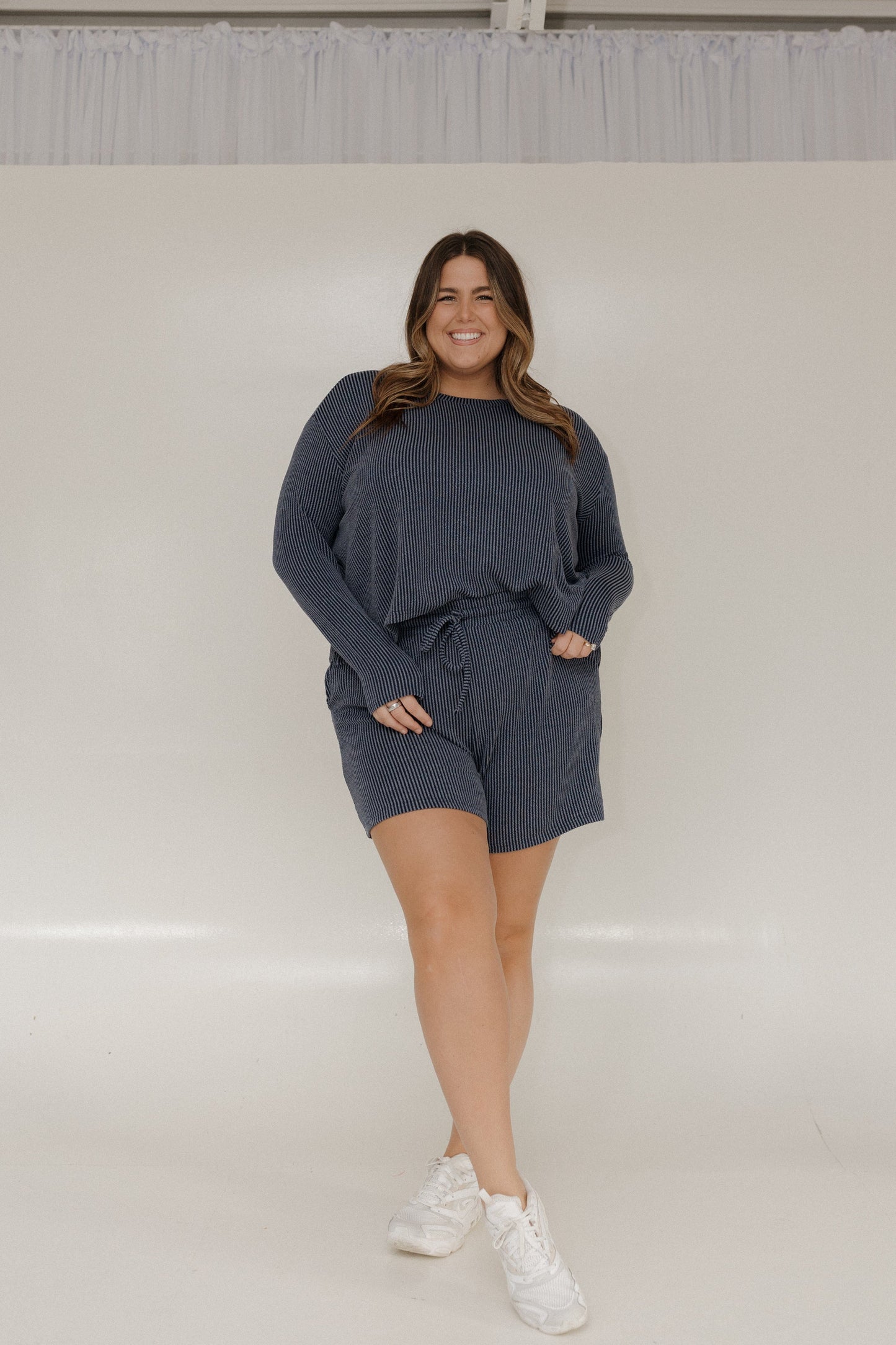 Woman wearing a dark gray outfit with shorts and a long-sleeve top on a white background