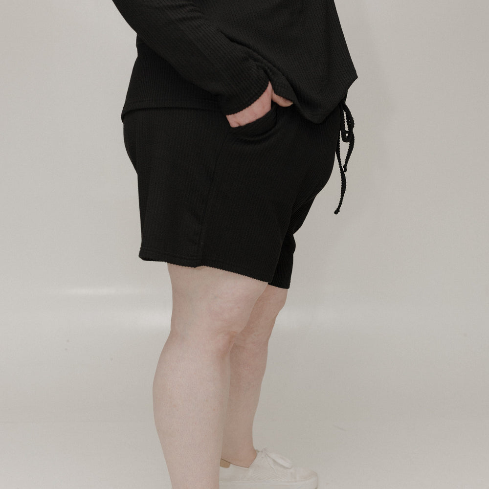 Person wearing a black outfit with white sneakers on a plain background