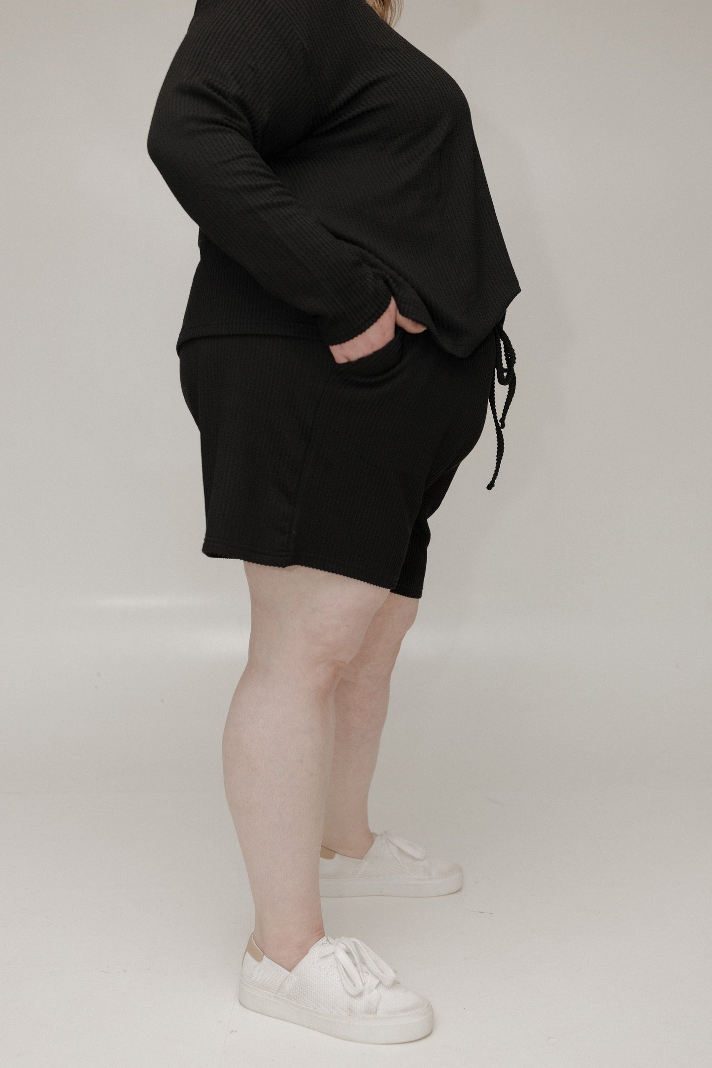 Person wearing a black outfit with white sneakers on a plain background