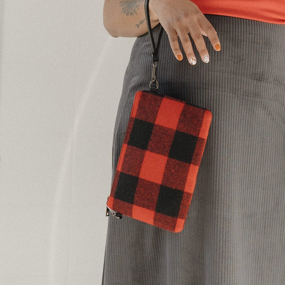 Person wearing a red shirt, gray skirt, and black boots holding a red and black checkered bag.