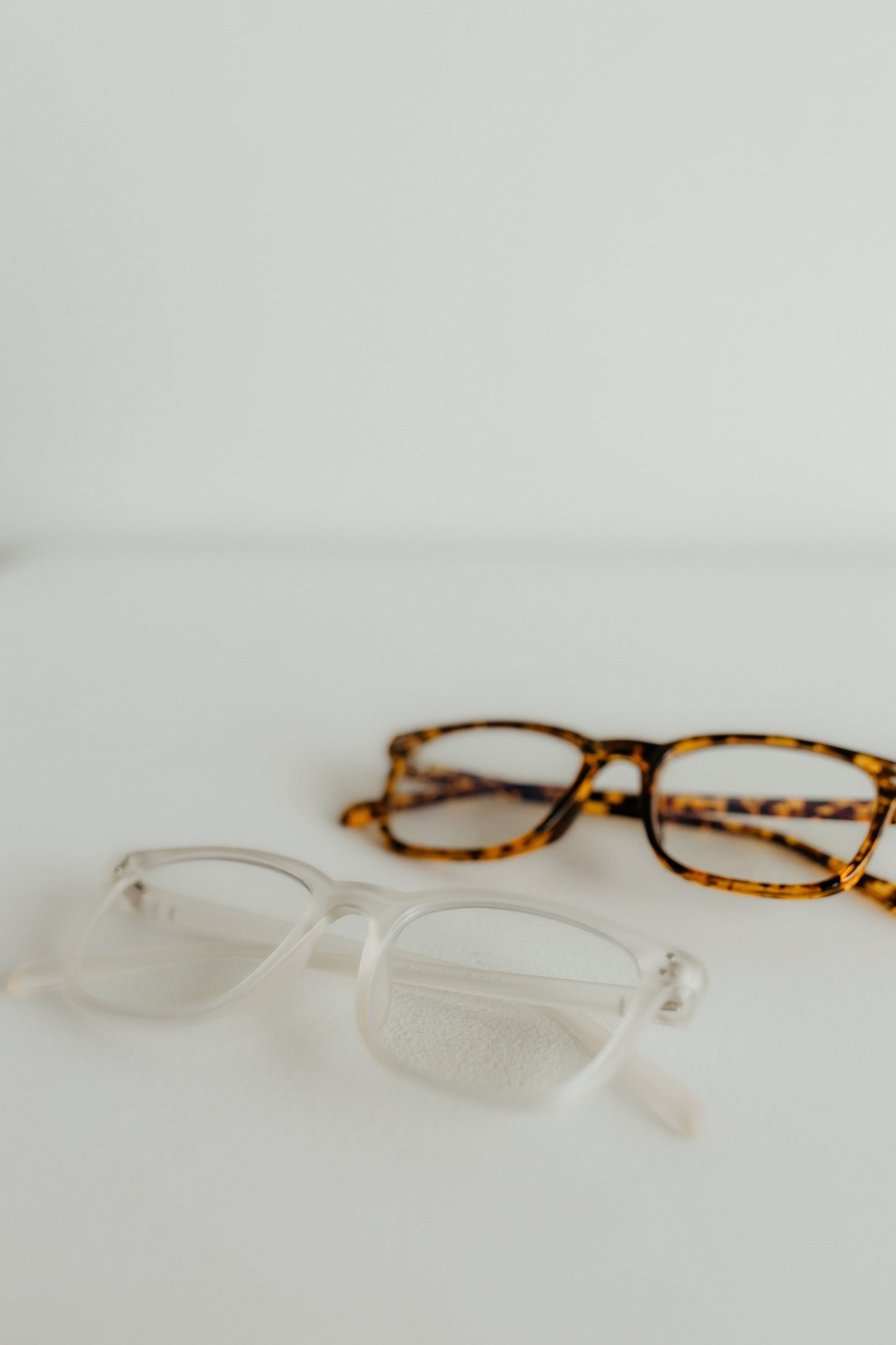 Two pairs of glasses, one with clear frames and the other with tortoiseshell pattern, on a light background.