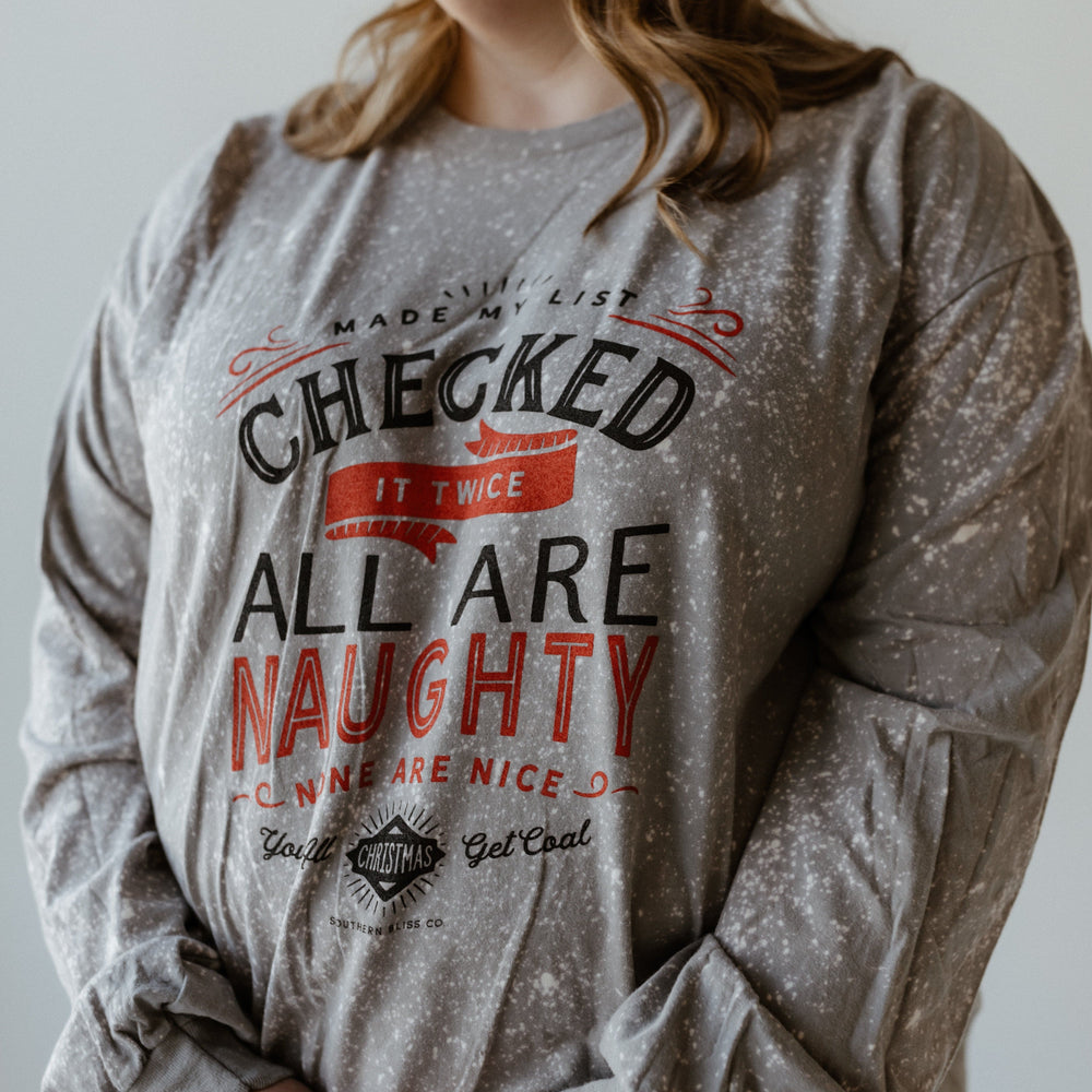 Person wearing a gray, hand-bleached sweater with the text: "Made the list, checked it twice, all are naughty, none are nice. Christmas get real." A funny graphic tee that captures the holiday spirit perfectly.