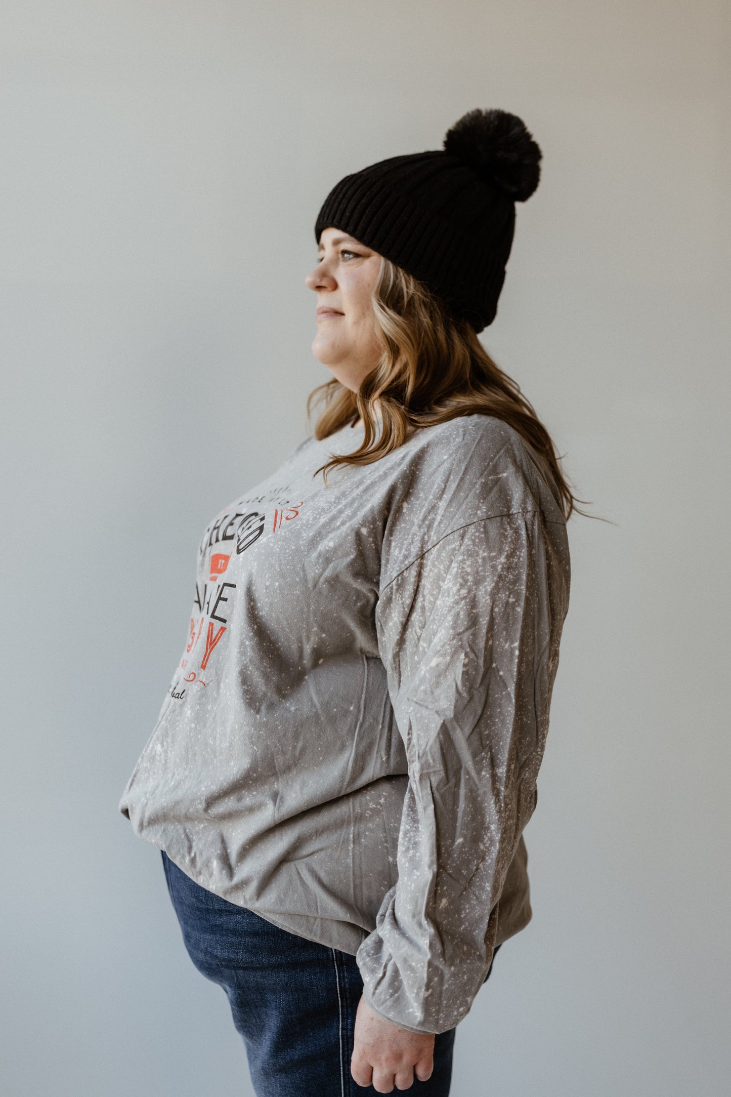 A person sporting a hand bleached gray shirt, black knit beanie, and jeans is standing sideways against a plain background.
