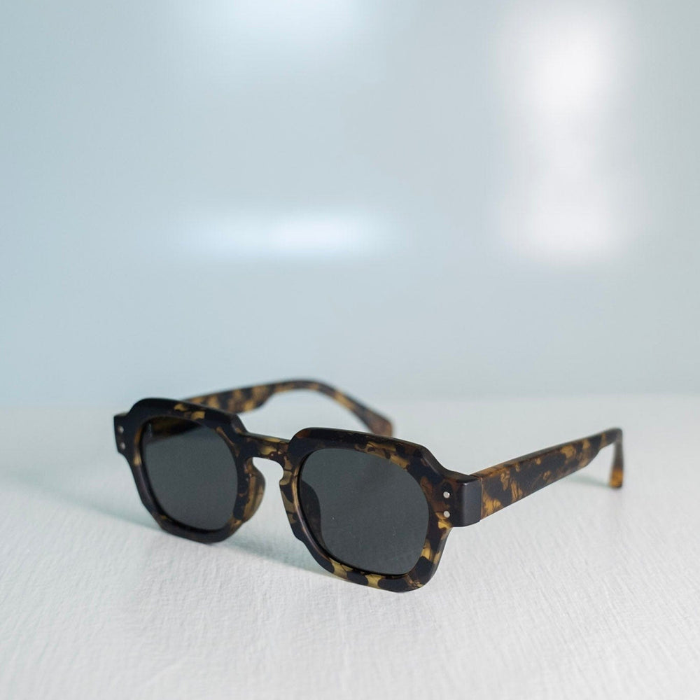 Sunglasses with tortoiseshell frame and dark lenses on a light gray background