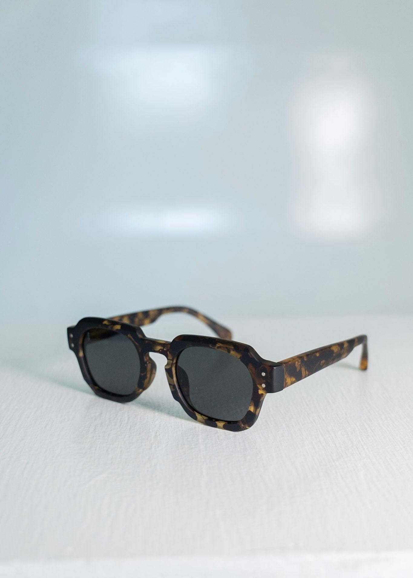 Sunglasses with tortoiseshell frame and dark lenses on a light gray background