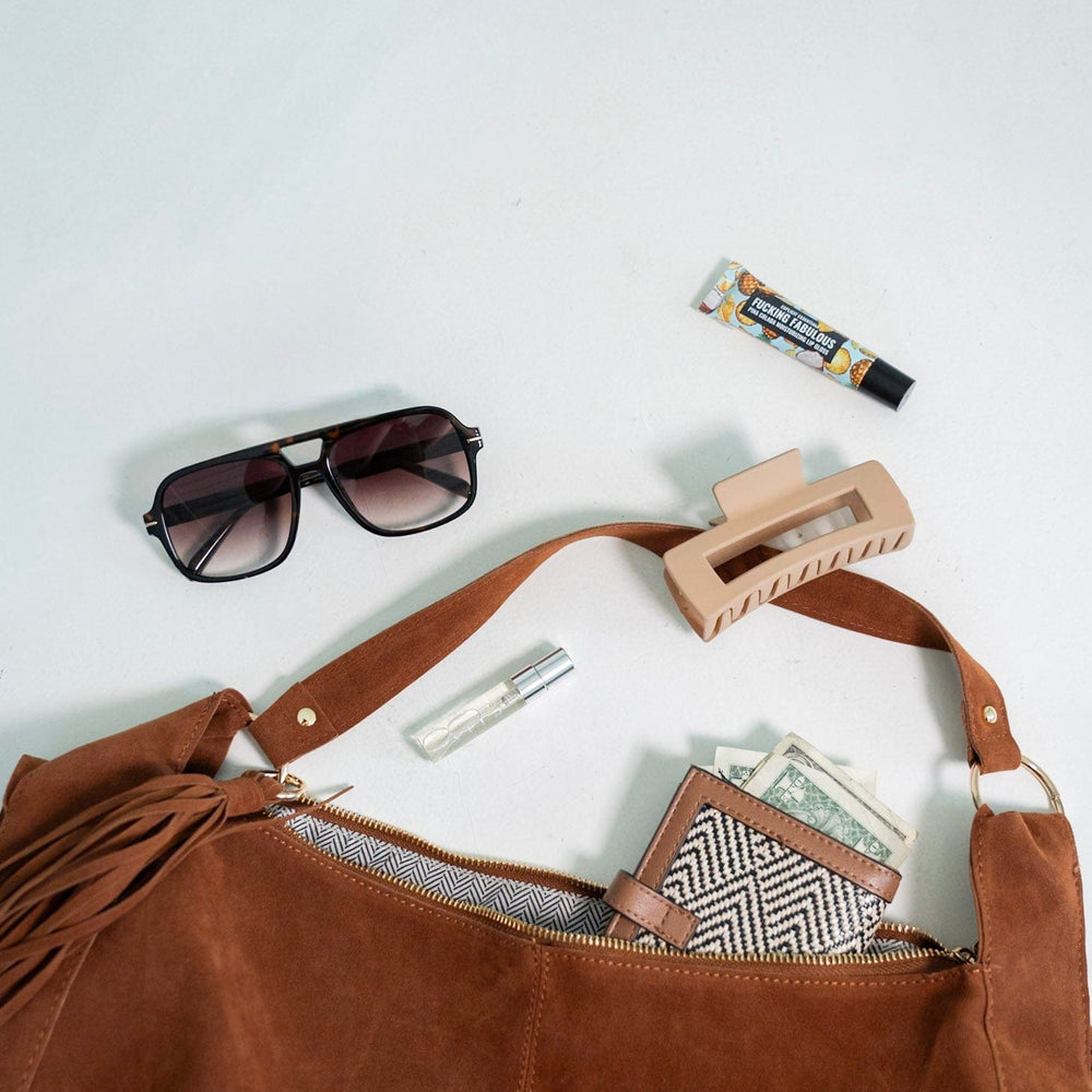 Brown leather bag with sunglasses, hair clip, and money on a white background