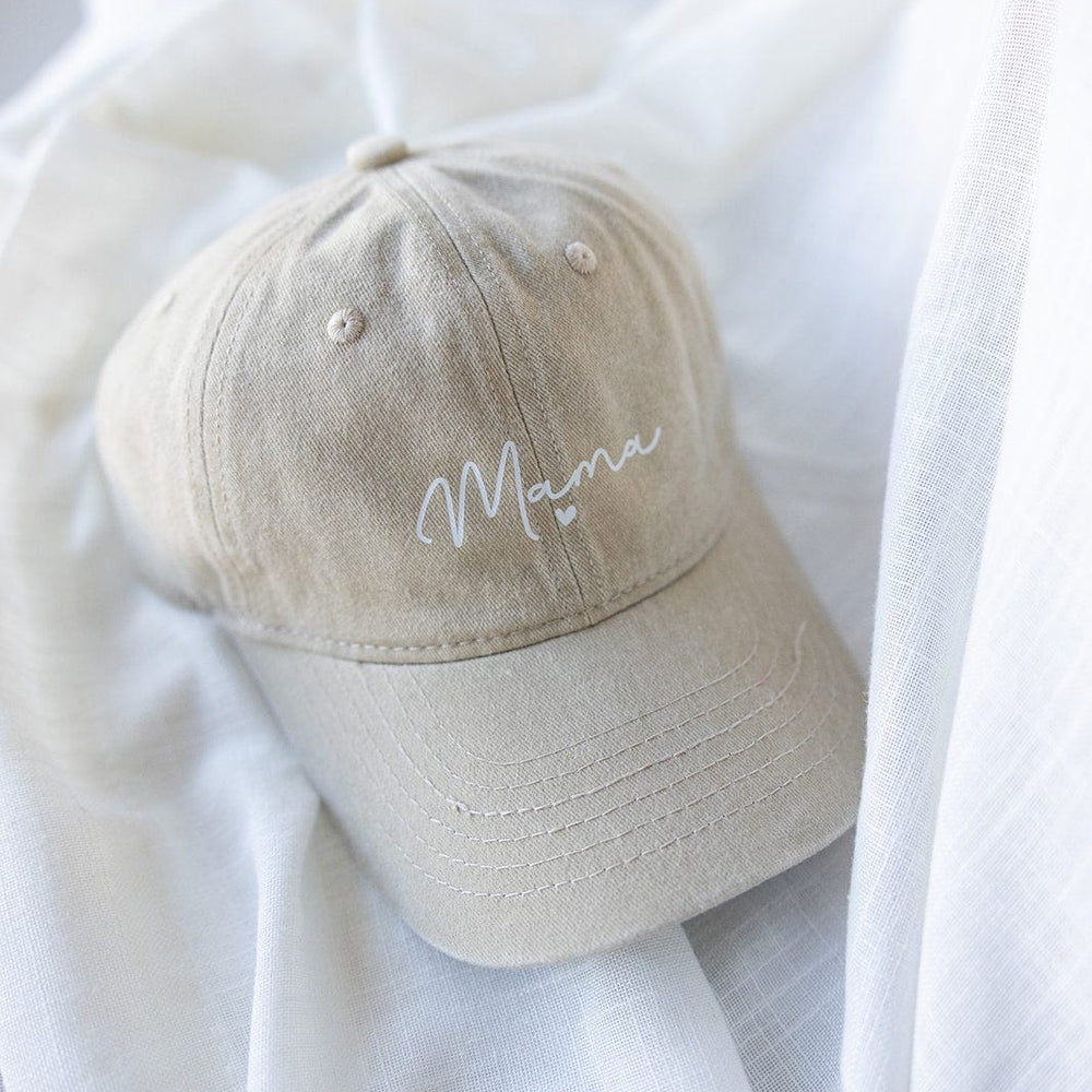 Beige MAMA Baseball Cap with "Mama" embroidered in white on the front, featuring an acid-washed design. Perfectly displayed on a soft white fabric, making it an ideal Mother's Day gift.