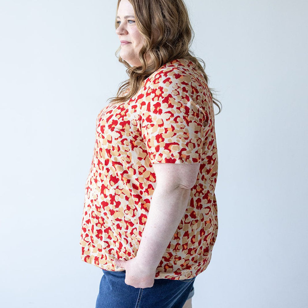 A person with long, wavy hair stands in profile wearing a MANDARIN COLLAR JERSEY KNIT BLOUSE from Love Marlow and denim shorts made of jersey knit fabric against a plain background.