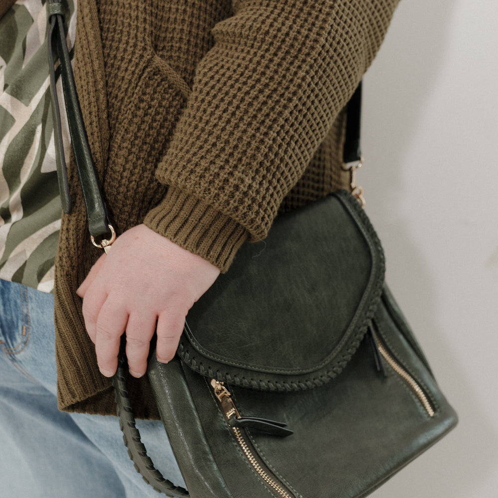 Person holding a green leather bag against a plain background