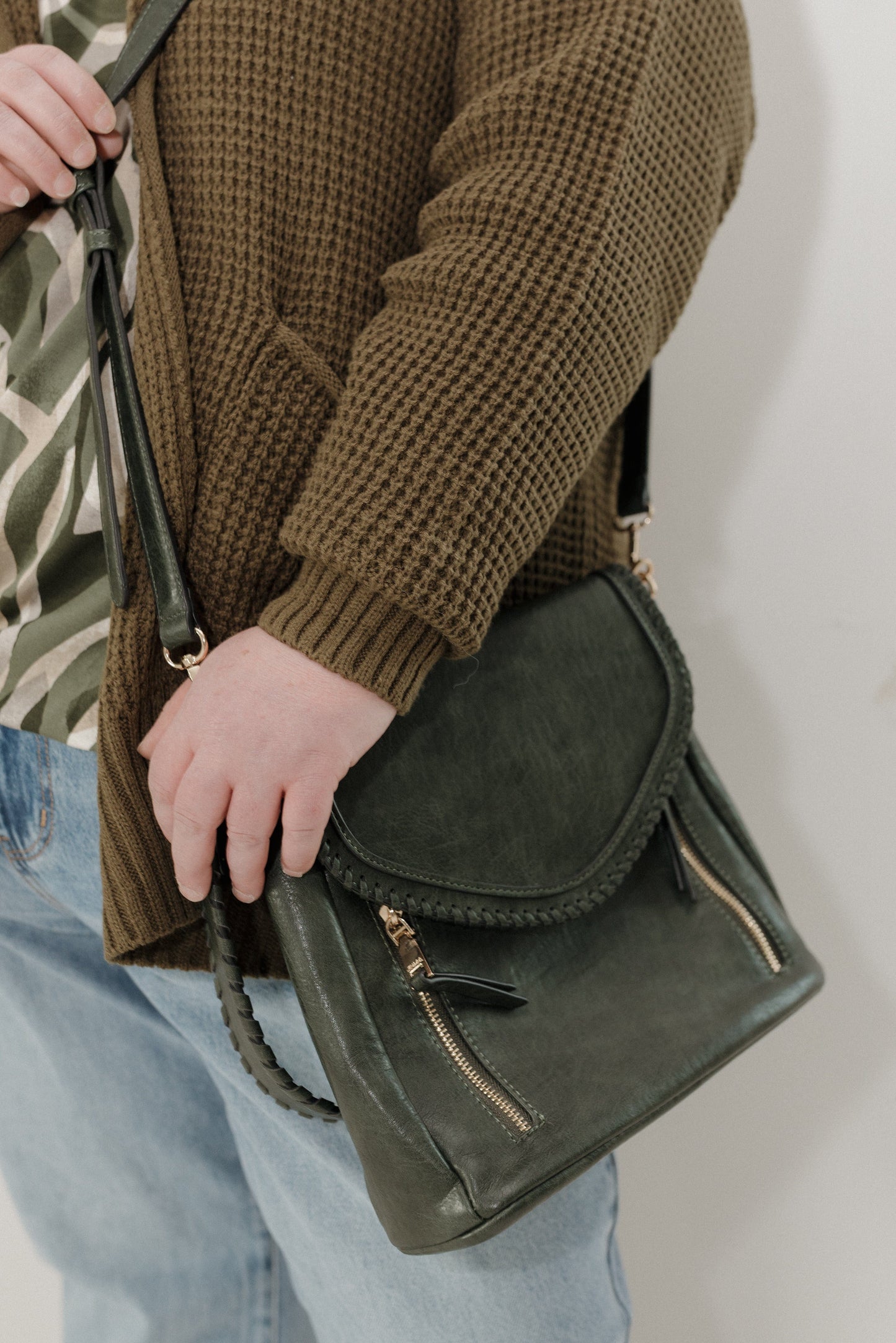 Person holding a green leather bag against a plain background