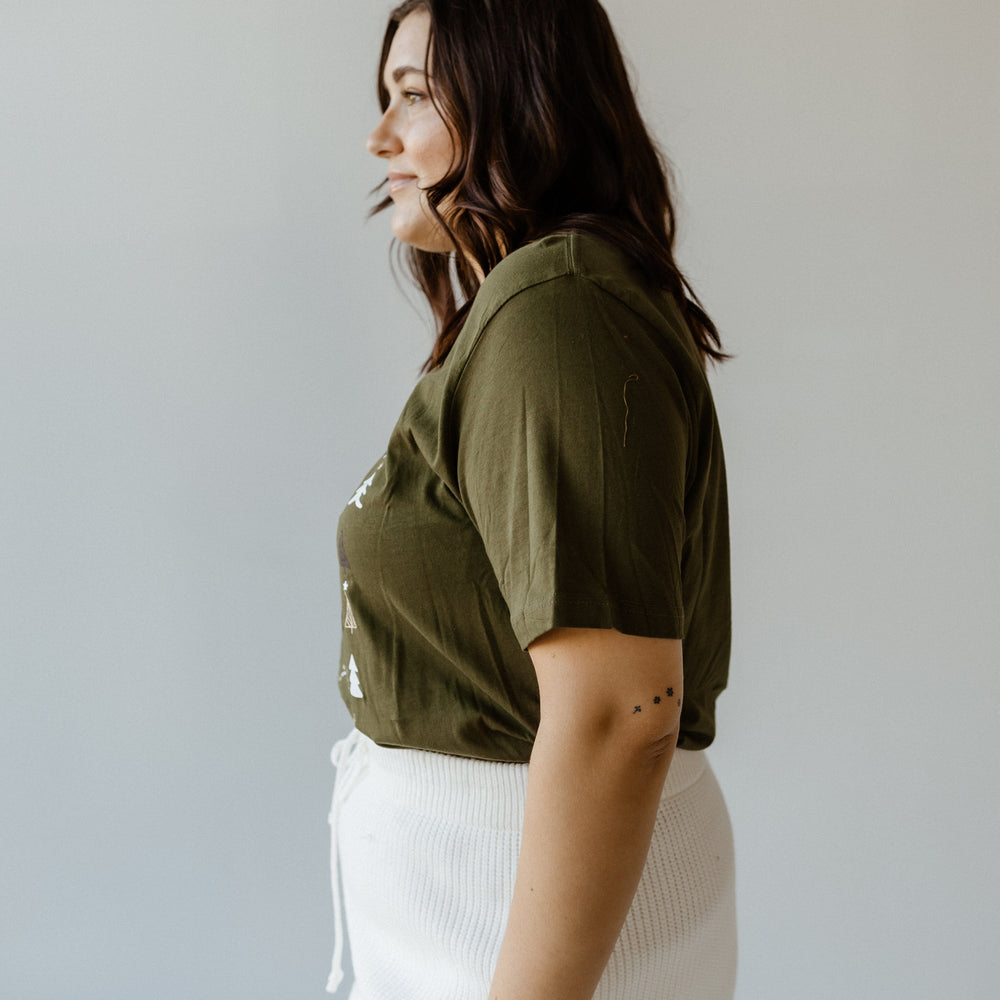 A person is standing in profile against a neutral background, embracing cozy style with a green shirt and white skirt that subtly reflects holiday spirit.