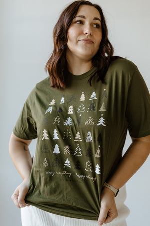 A person embraces the holiday spirit in a cozy style, sporting a green Christmas tee adorned with a tree pattern and the cheerful message "merry everything & happy always.