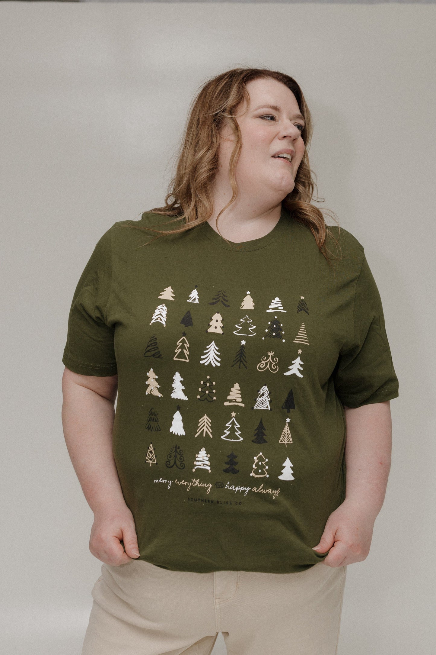 Person wearing an olive green t-shirt with tree patterns on a plain background