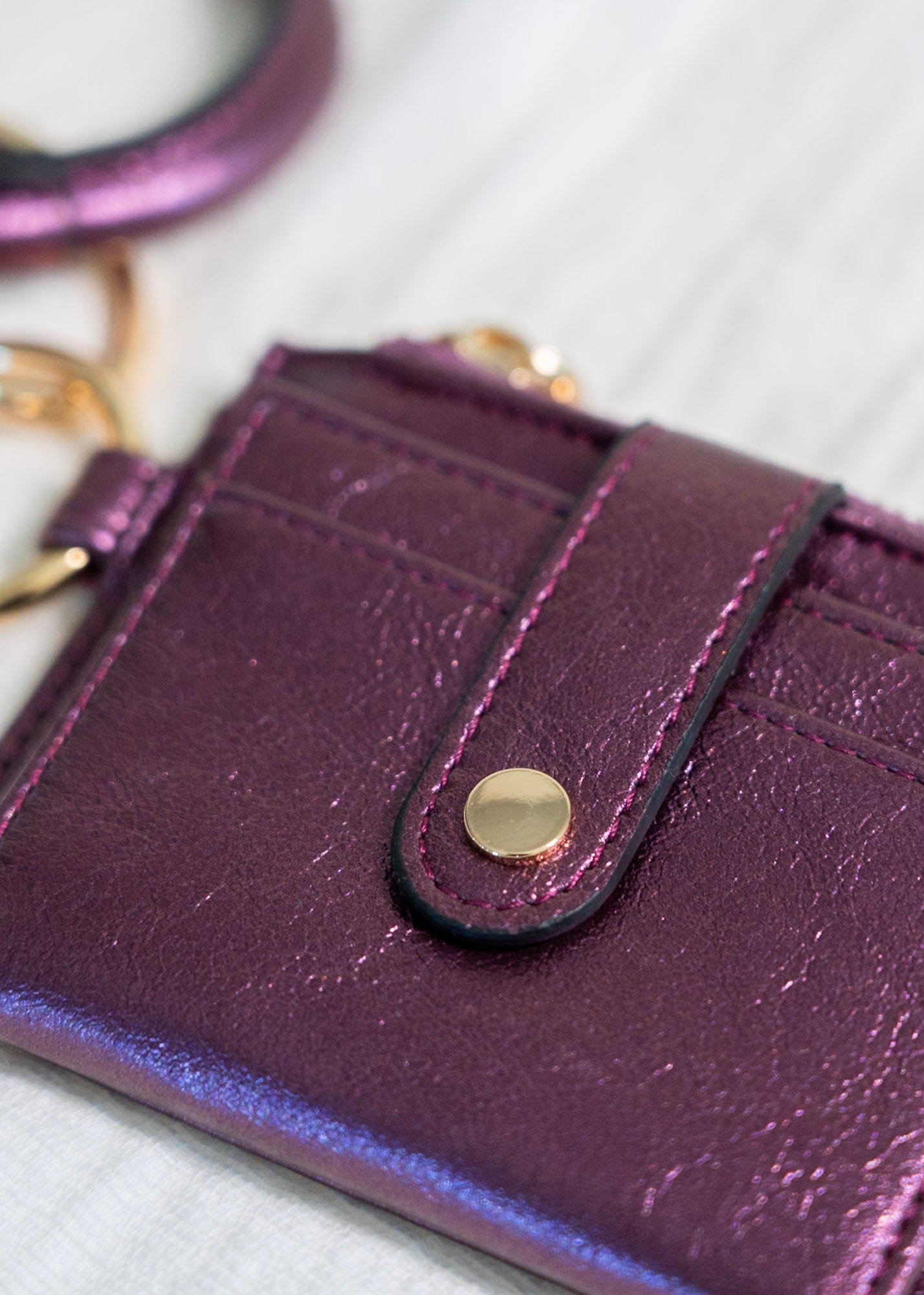 Show off your style with this metallic bangle wristlet wallet. Fold out the wallet to access your cards and IDs in secure snap closure — saving you from the rummage. Zip up your change pocket for a chic, sophisticated finish. Throw it on your wrist for easy access with an amethyst accent!